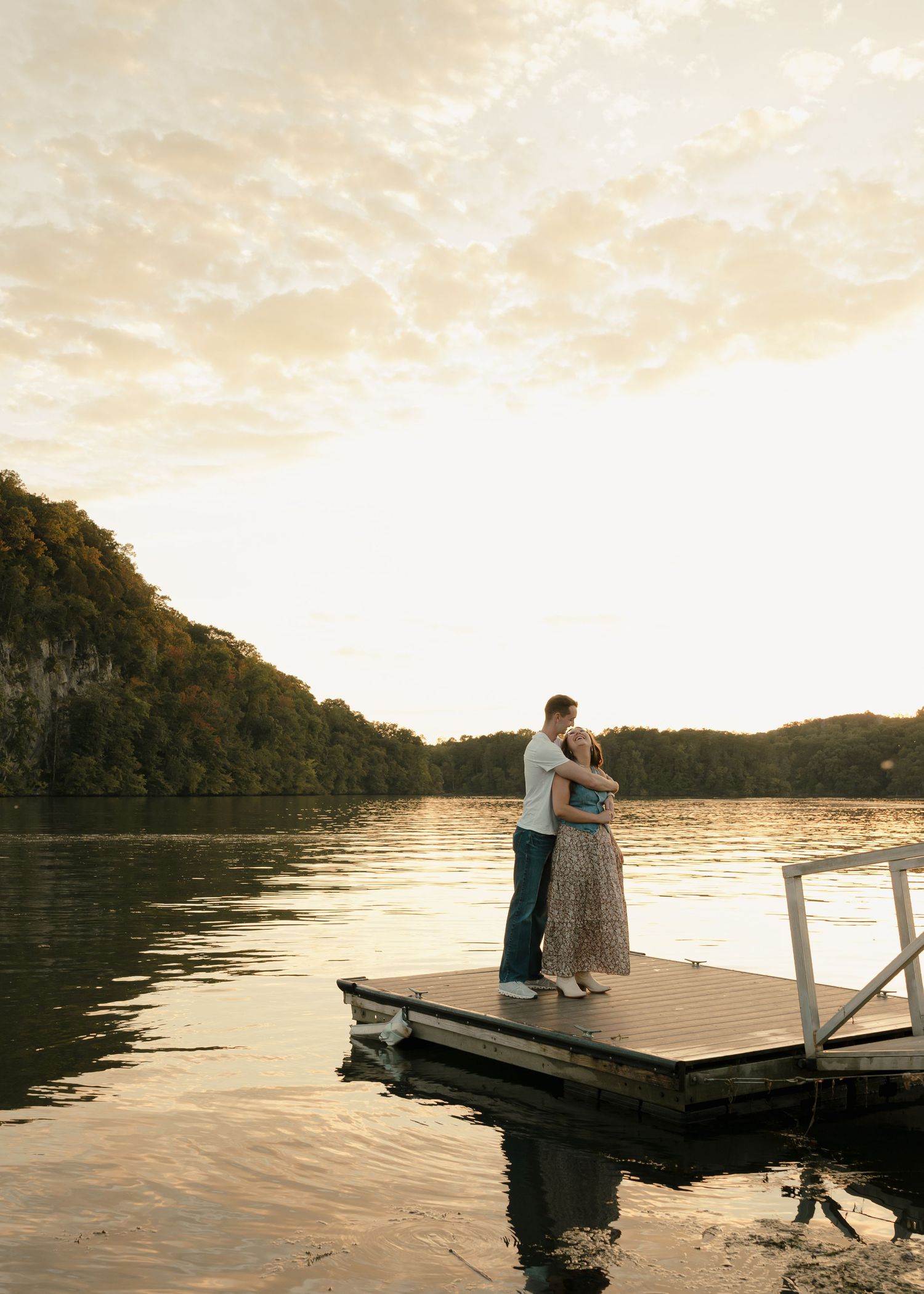 Romantic couple holding each other on a lake dock during golden hour sunset.
