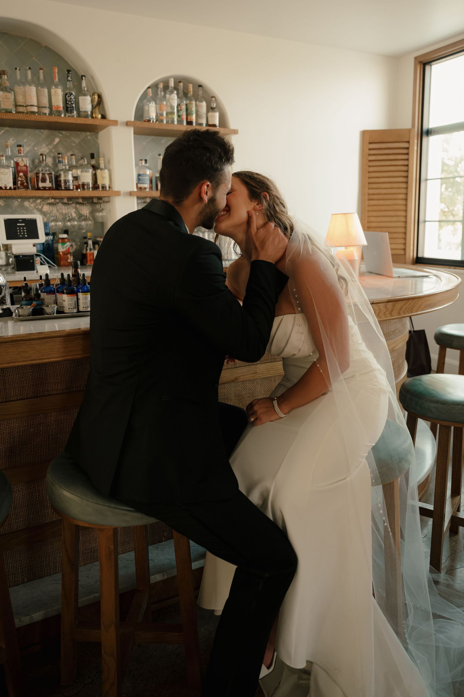 Bride and groom sharing a romantic kiss at a bar during their wedding reception.