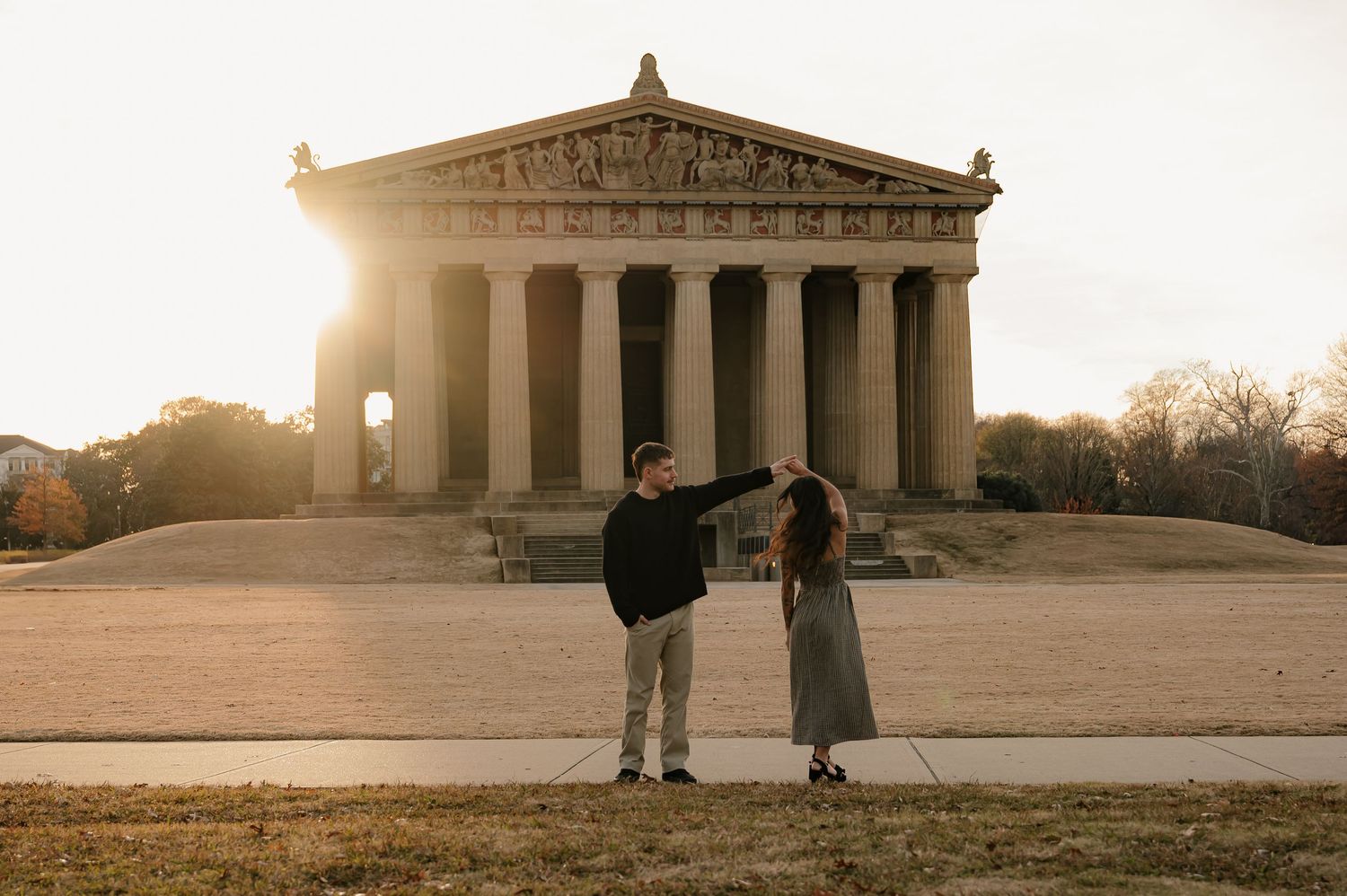 Couple dancing hand in hand at sunset in front of the Parthenon replica in Nashville, Tennessee.