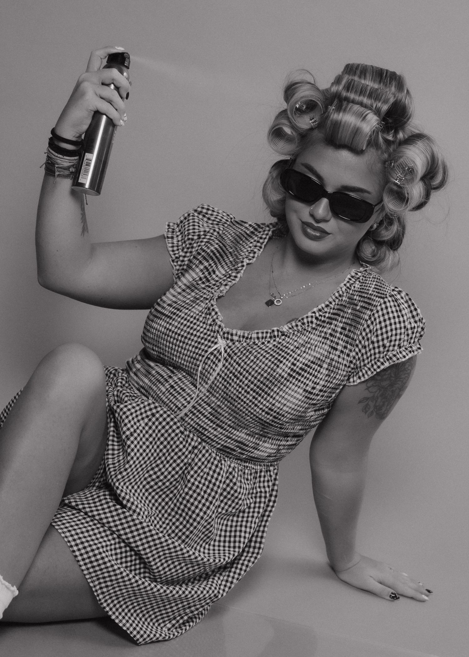 Retro-styled woman in curlers and sunglasses holding hairspray in black and white.