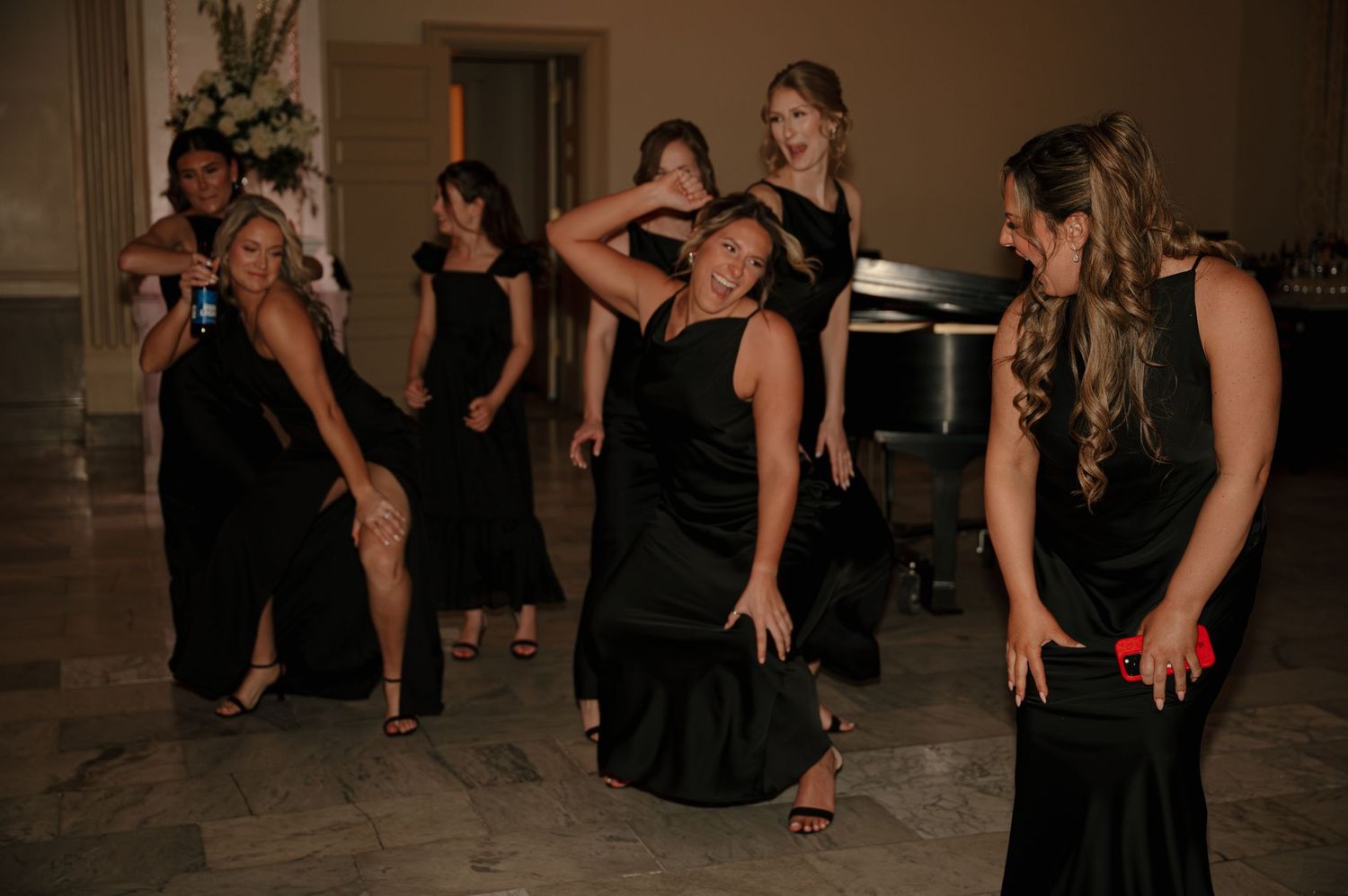 Bridesmaids in black velvet gowns dancing and celebrating joyfully at an elegant wedding reception.