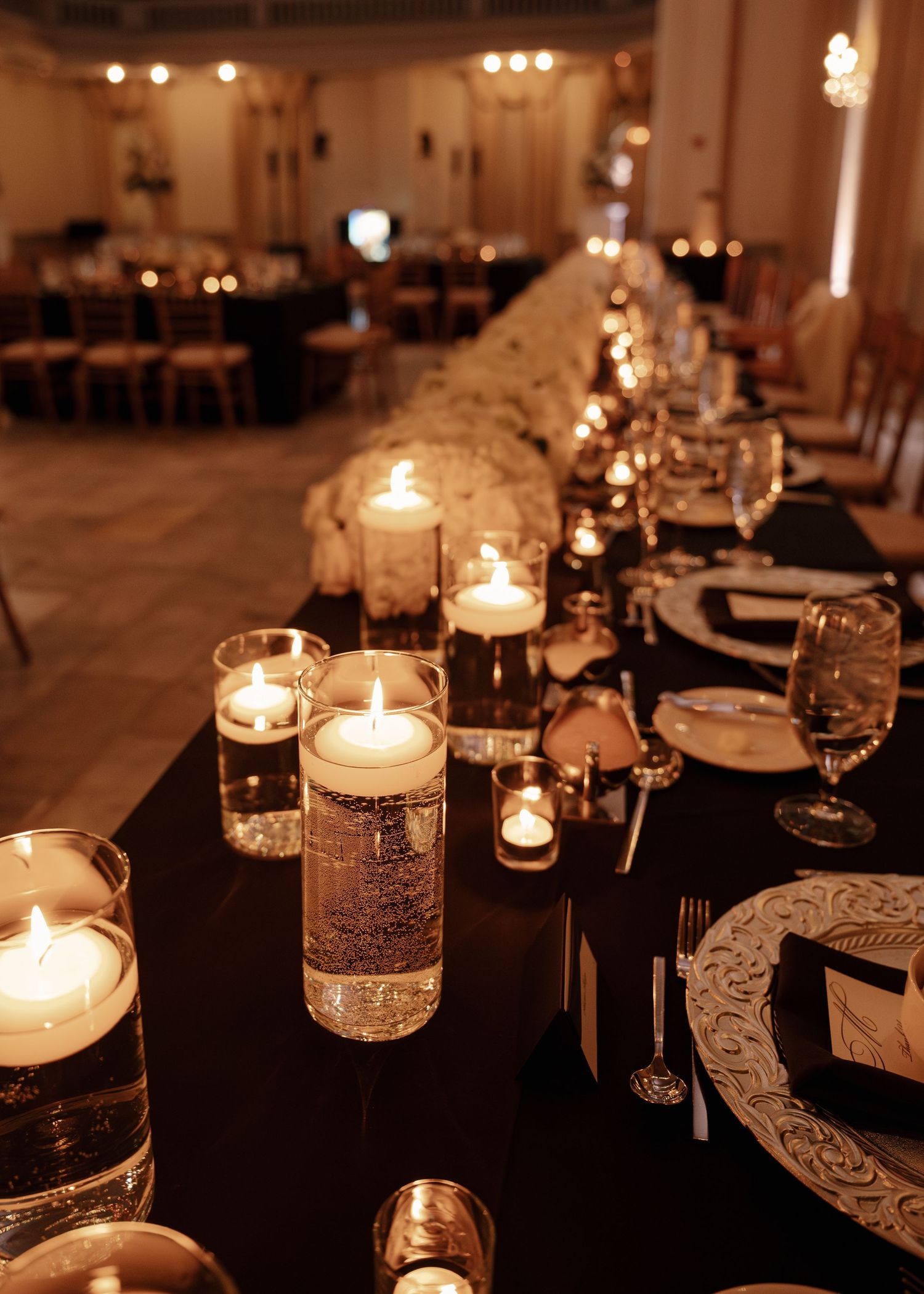 Elegant wedding reception table with floating candle centerpieces and black linen runner.
