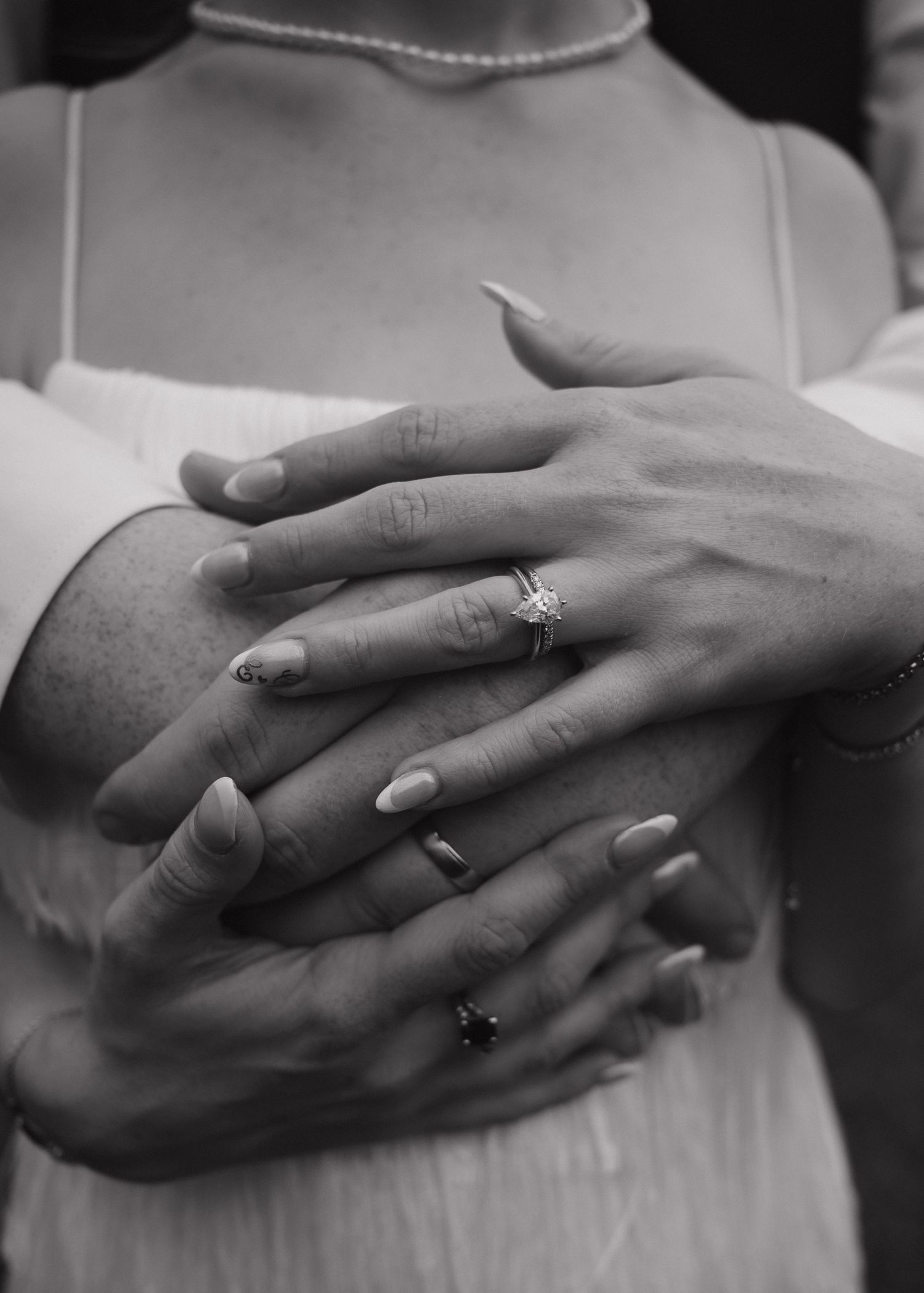 Close-up black and white photo of bride and groom hands with diamond engagement ring.