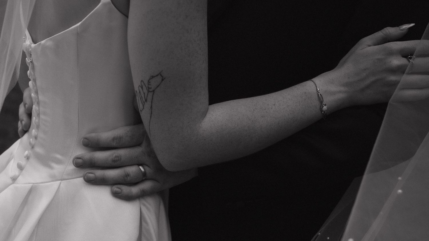Black and white close-up of groom holding bride with tattoo visible on her arm.