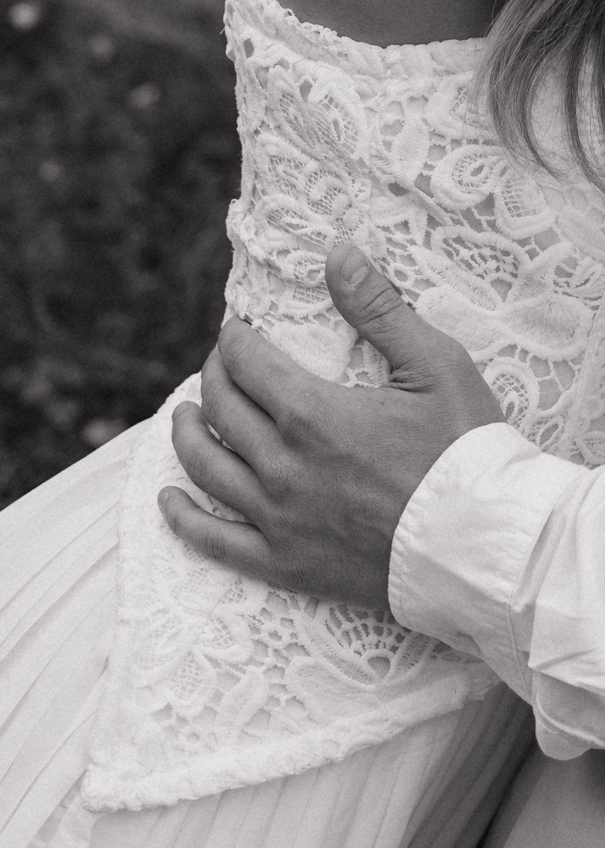 Black and white close-up of a groom's hand on a bride's lace wedding dress waist.