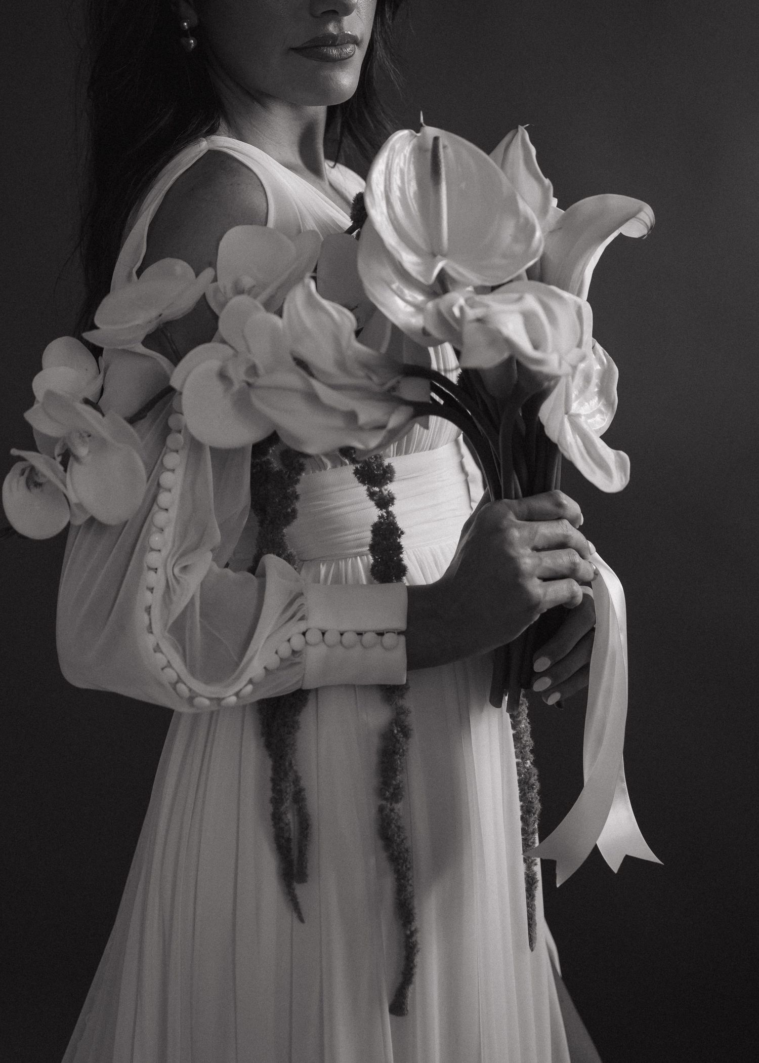 Black and white photo of woman in white gown holding large bouquet of tropical flowers and stylish handbag.