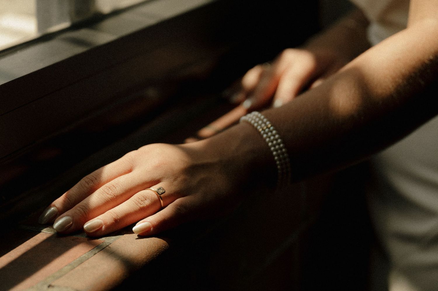 Close-up of bride's hand with engagement ring and pearl bracelet on a railing.