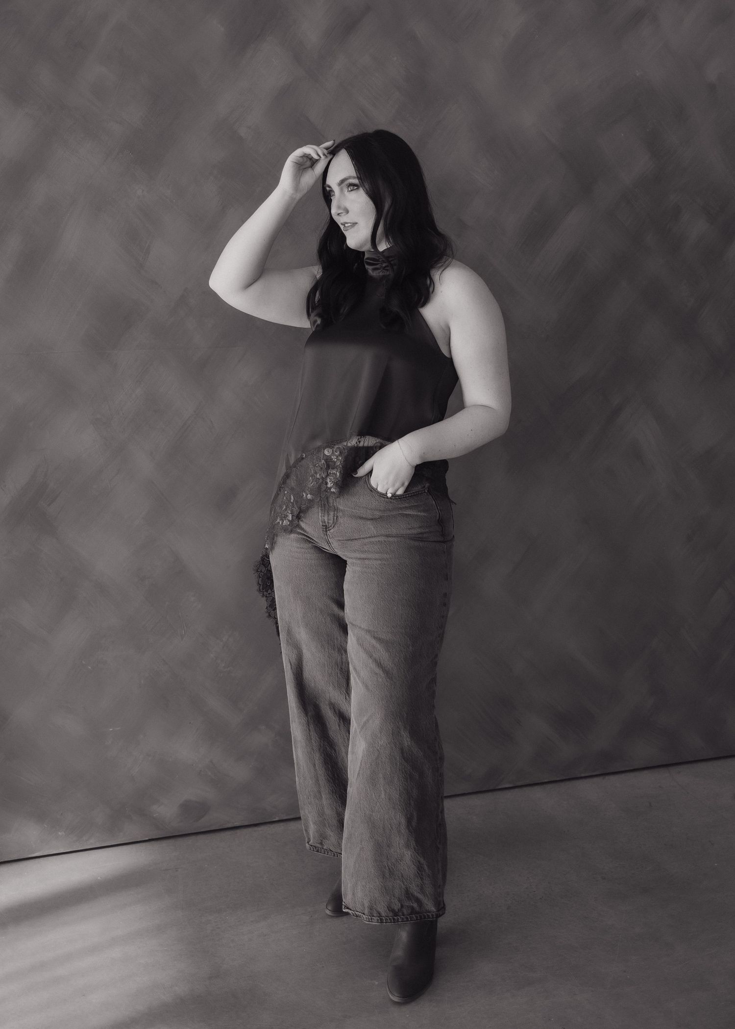 Black and white portrait of brunette woman in sleeveless top and jeans posing confidently.