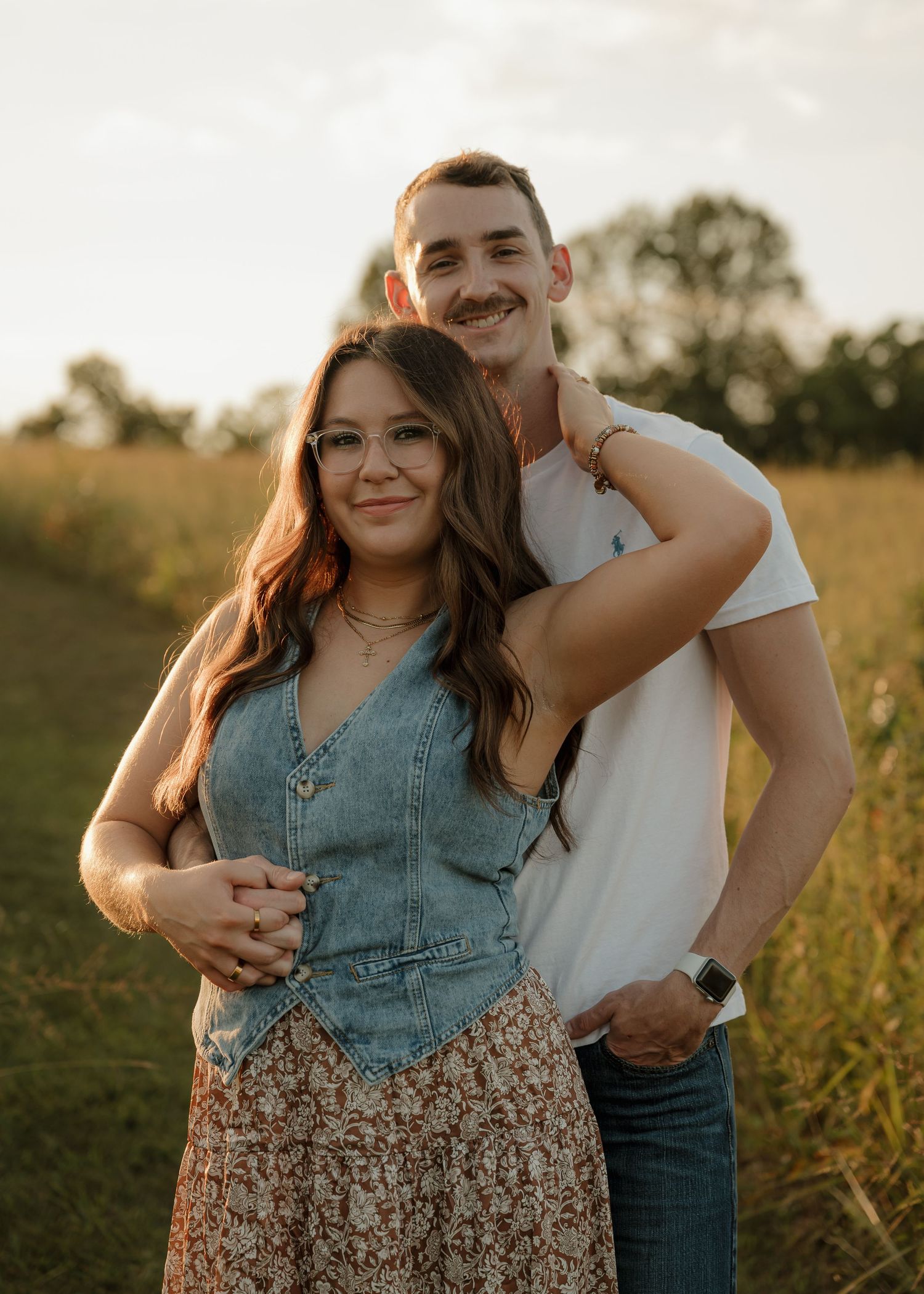 Smiling couple posing together in a golden meadow at sunset.
