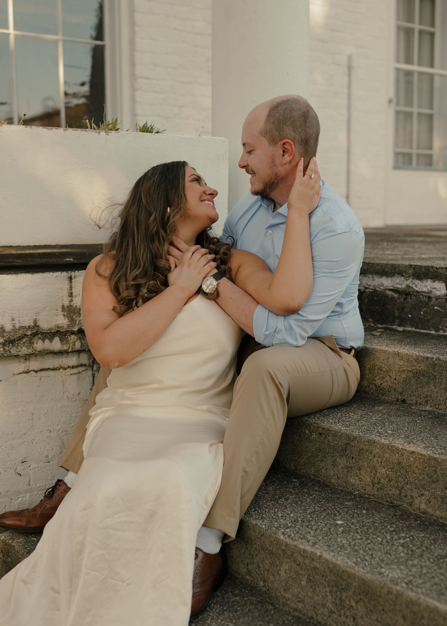 Smiling bride and groom sitting together on stone steps sharing a joyful romantic moment.