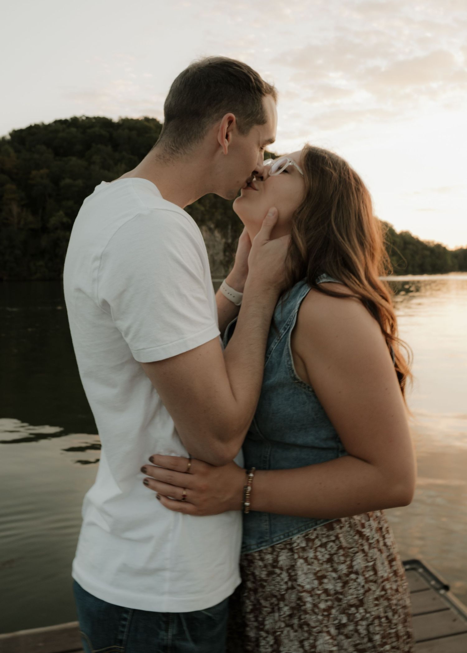 Couple sharing a tender kiss on a lakeside dock at sunset.