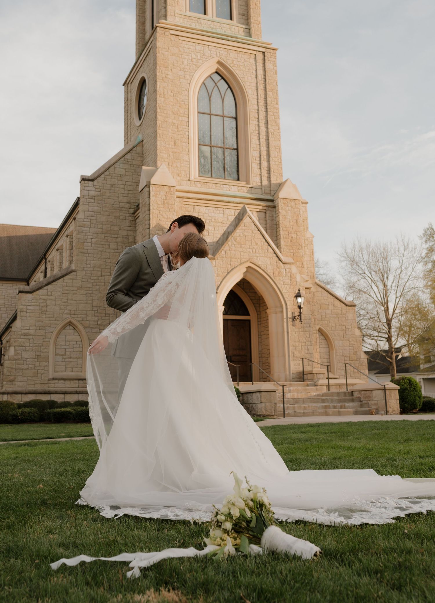 Groom dipping bride in a romantic kiss outside a stone Gothic church with a sweeping veil.
