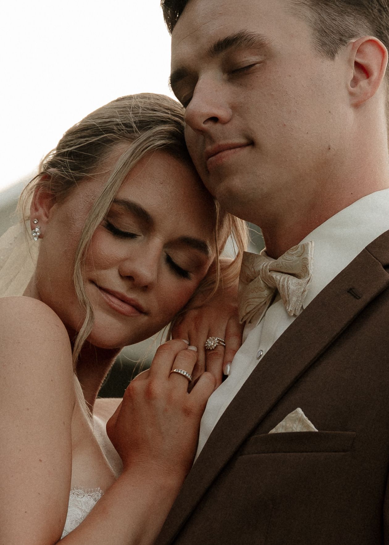 Close-up of bride resting head on groom's shoulder showing diamond engagement ring and wedding band.