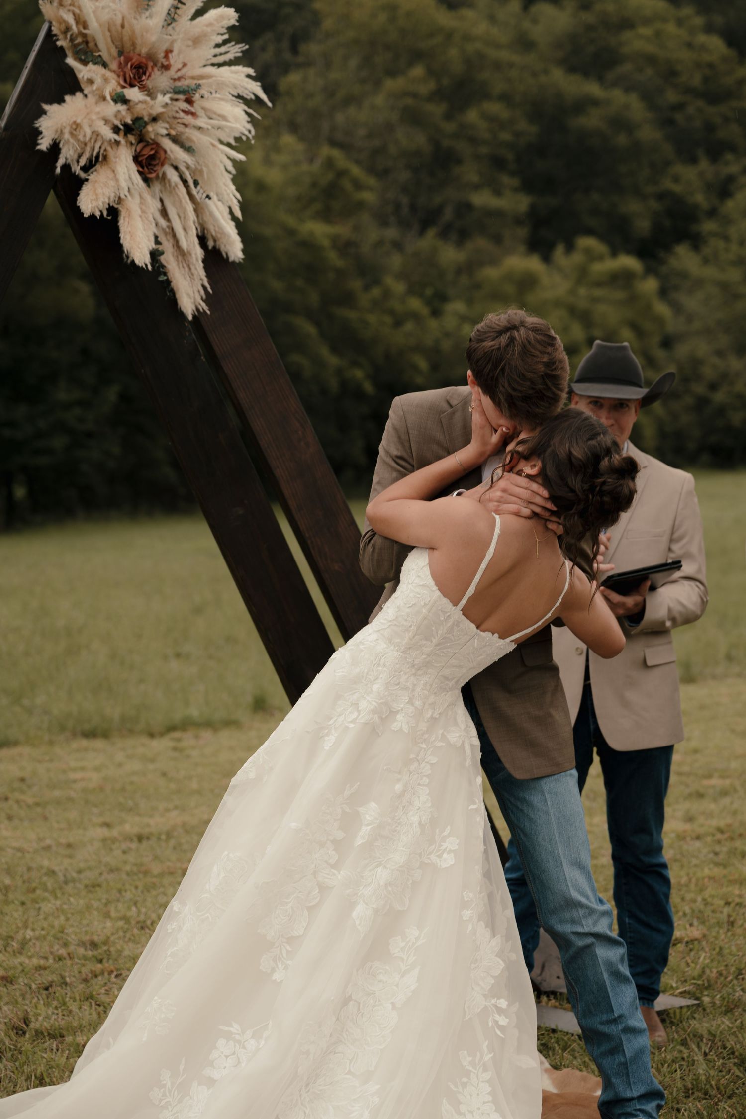 Bride and groom sharing first kiss at outdoor boho wedding ceremony.