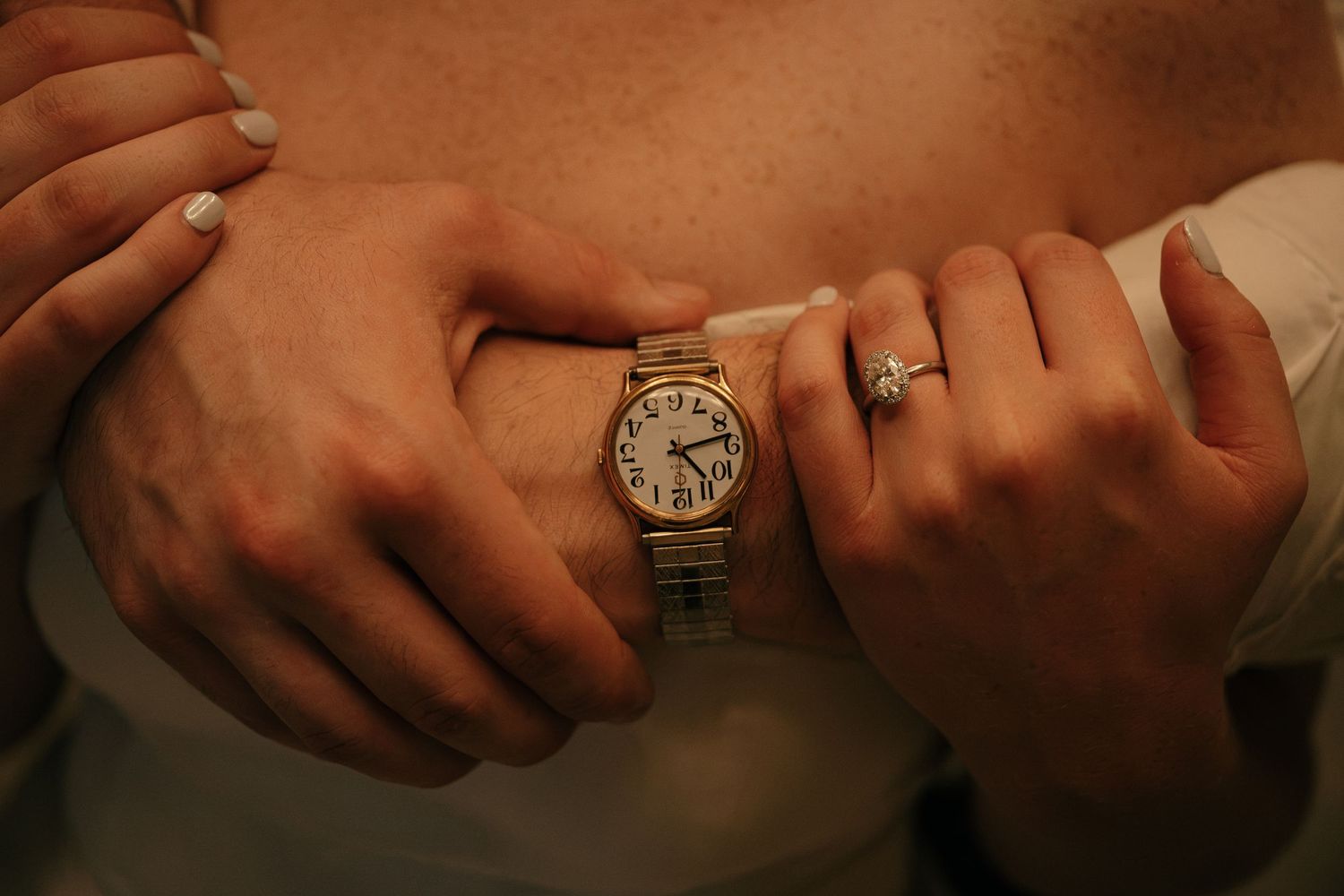 Close-up of hands embracing, featuring a gold Cartier watch and a diamond engagement ring.