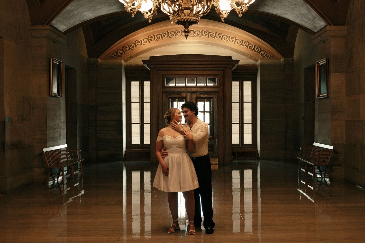 Couple dancing romantically in elegant stone hall with chandelier and arched doorway.