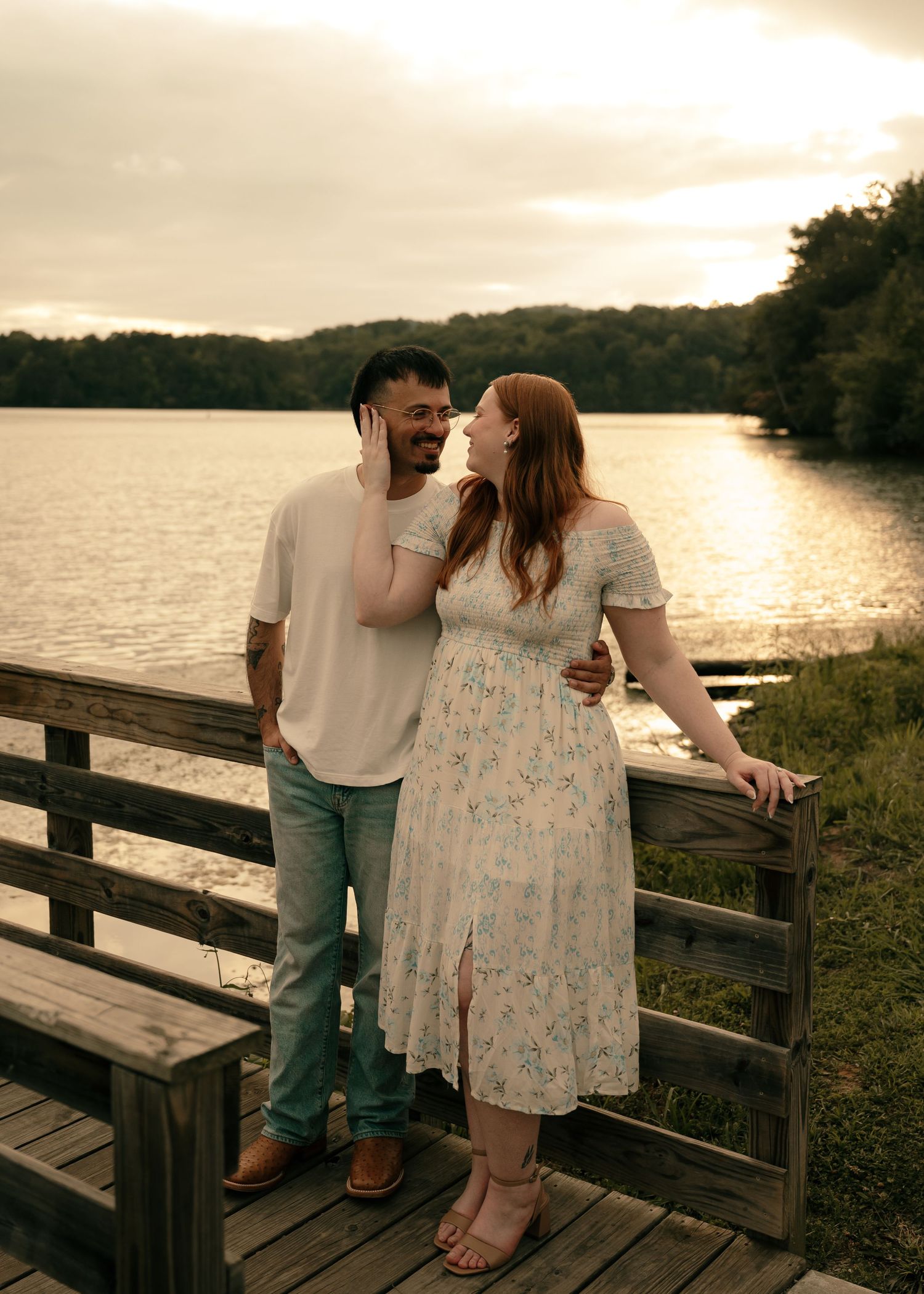 Couple sharing a romantic moment on a wooden dock by a lake at golden sunset.