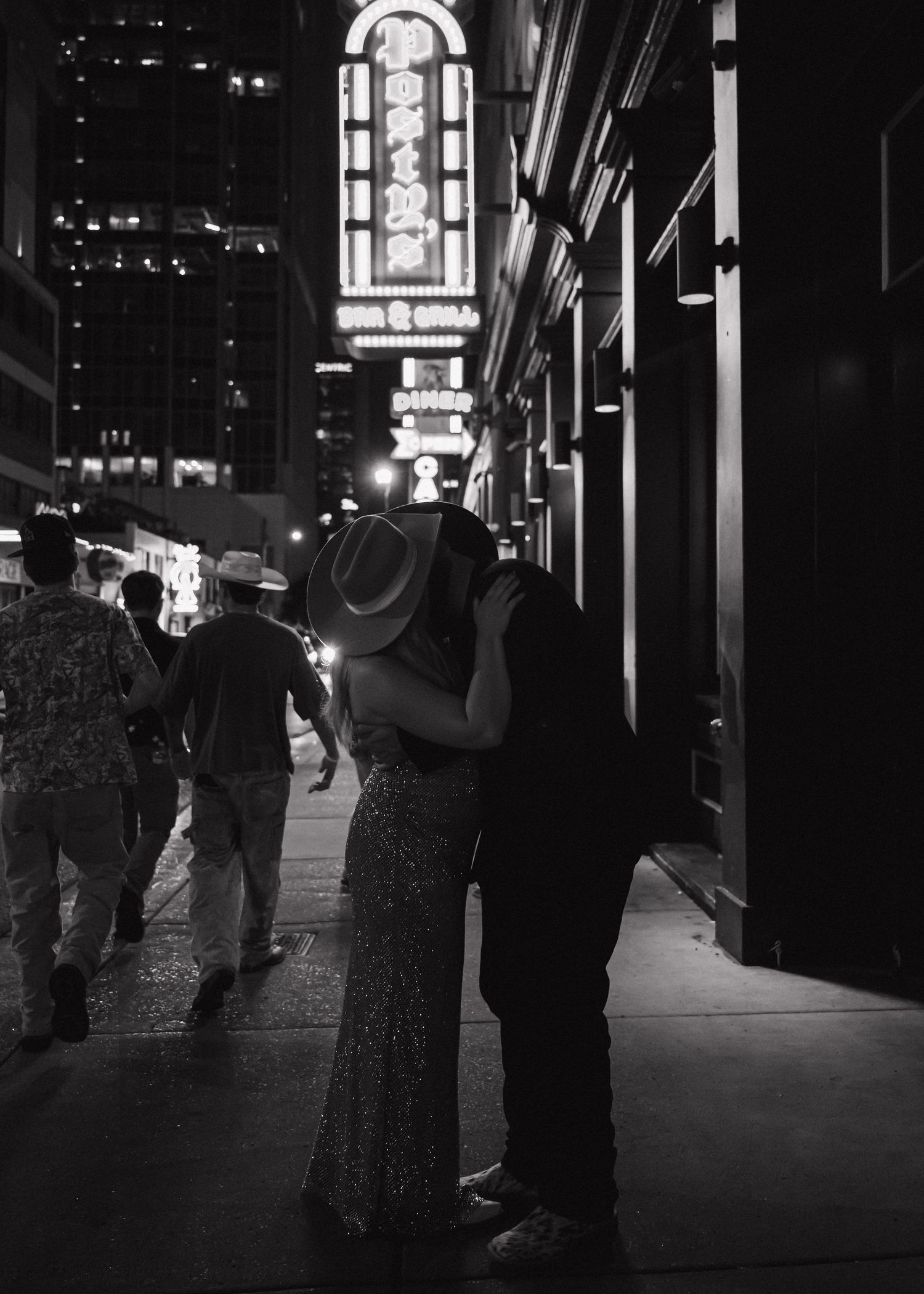 Couple kissing on a bustling city street at night, with neon signs glowing in the black and white background.