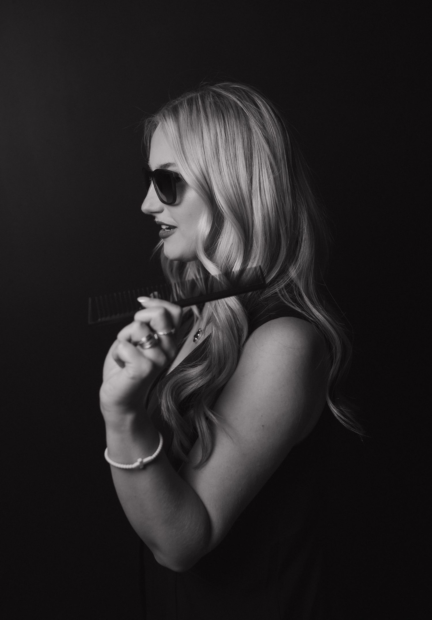 Blonde woman in black top and sunglasses in dramatic black and white profile portrait.