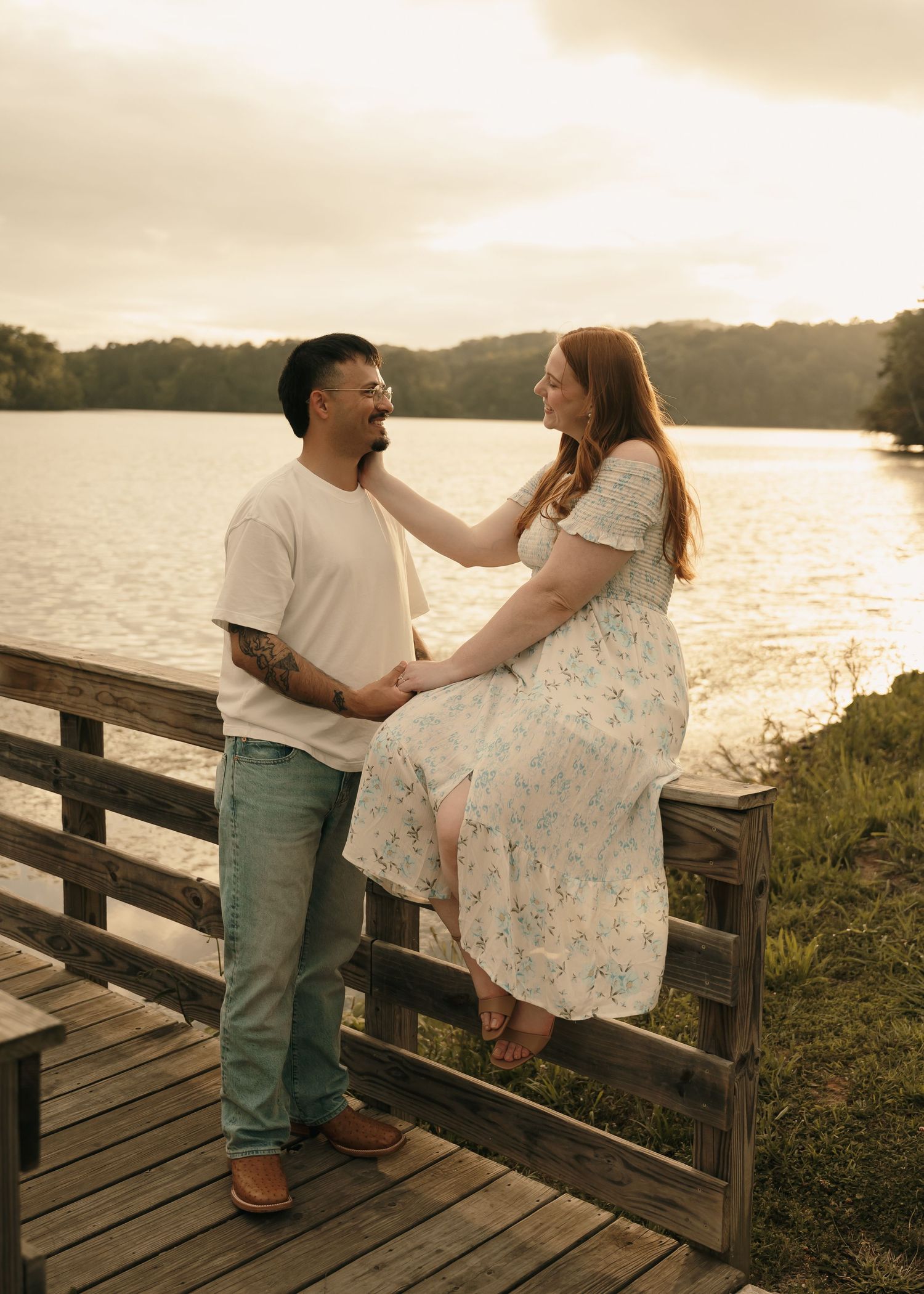 Couple sharing a romantic moment on a wooden dock by a lake at golden hour sunset.