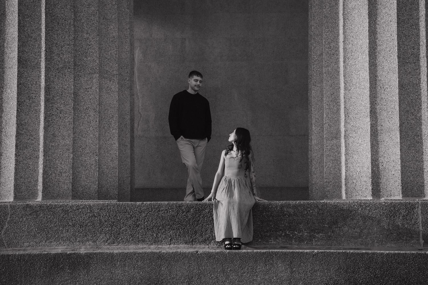 Black and white photo of couple standing apart on steps between tall columns.