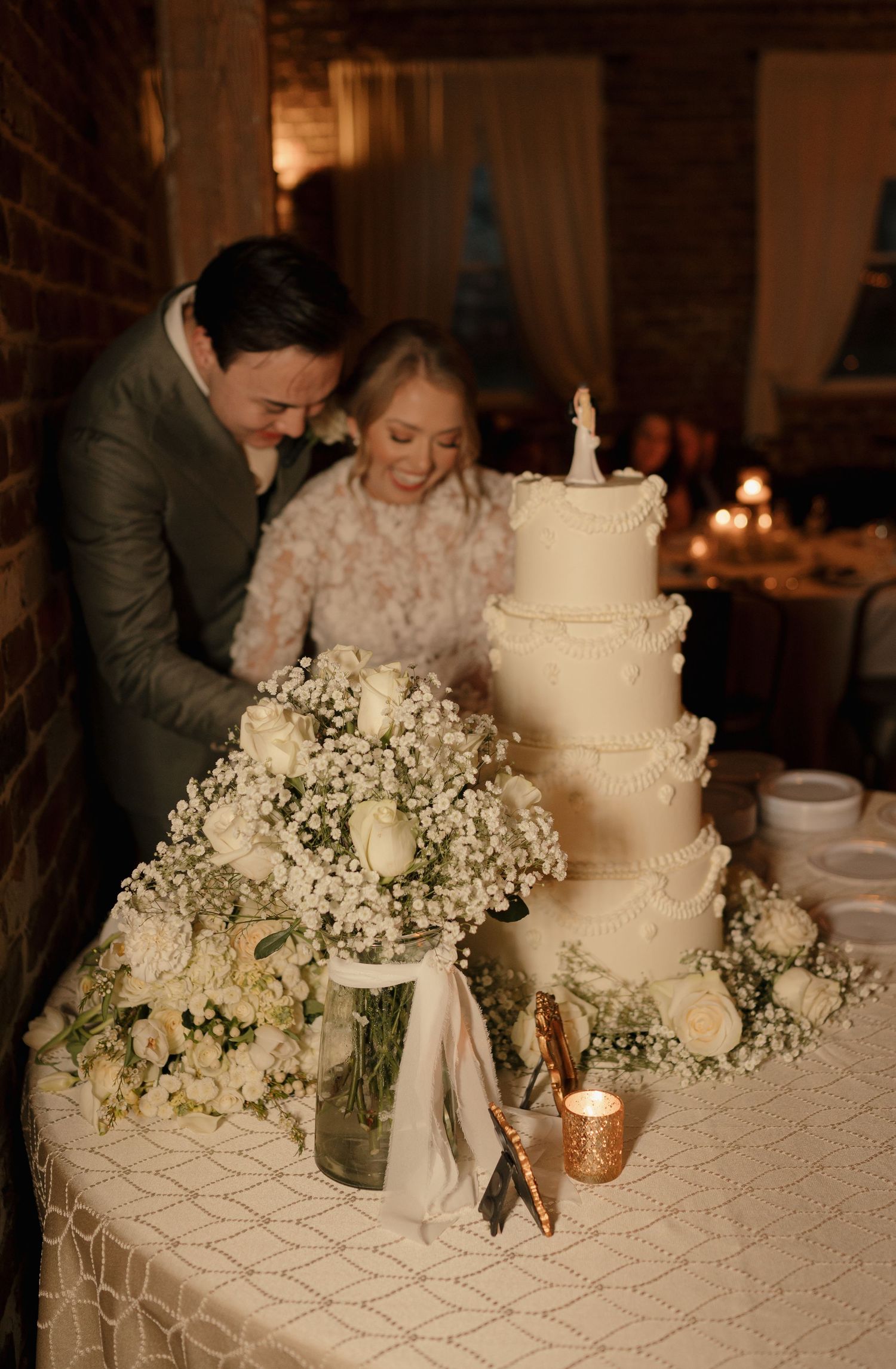 Smiling bride and groom standing beside a four-tier white wedding cake with floral arrangements.