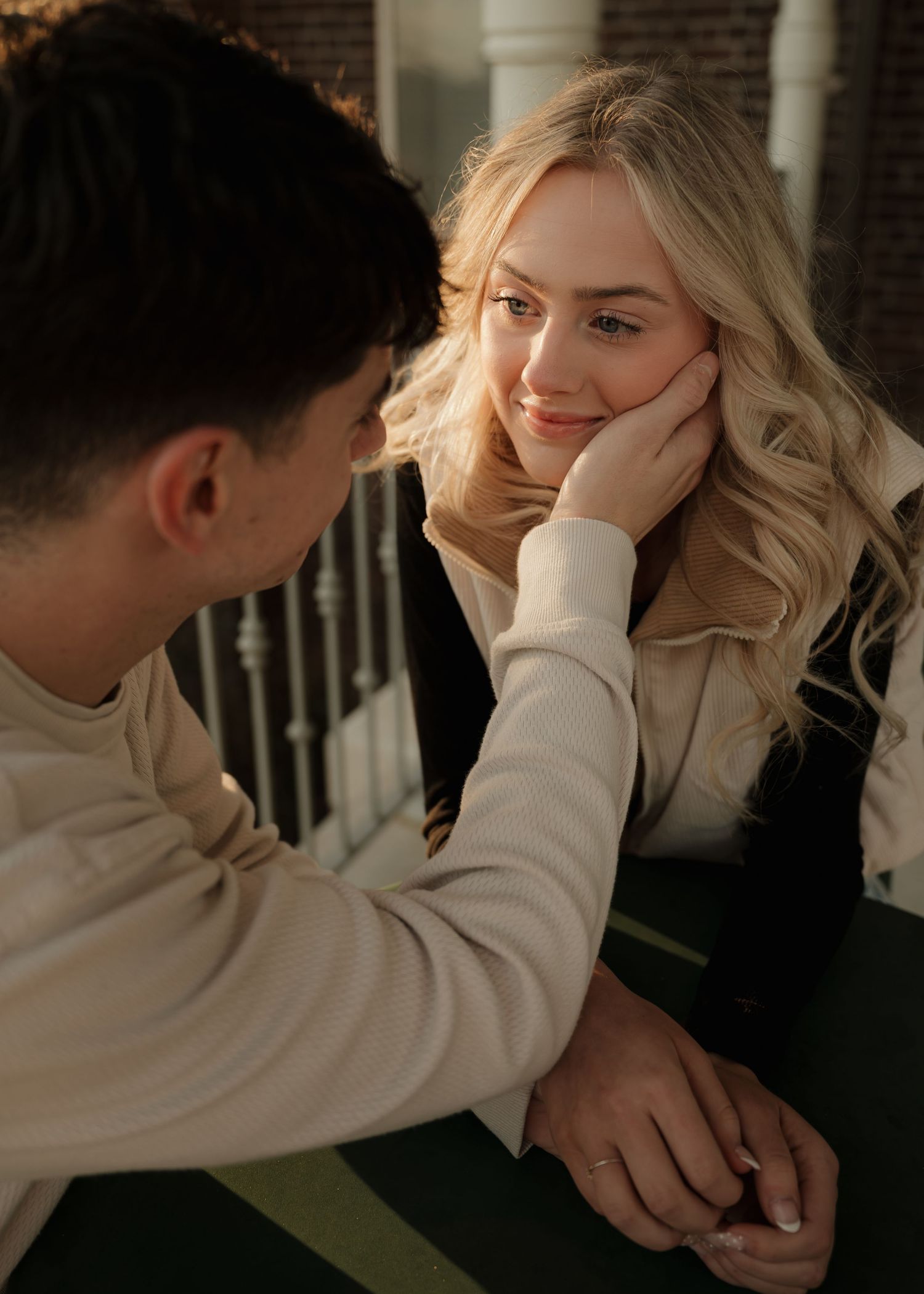 A man tenderly touches a smiling blonde woman's face during a romantic outdoor moment.