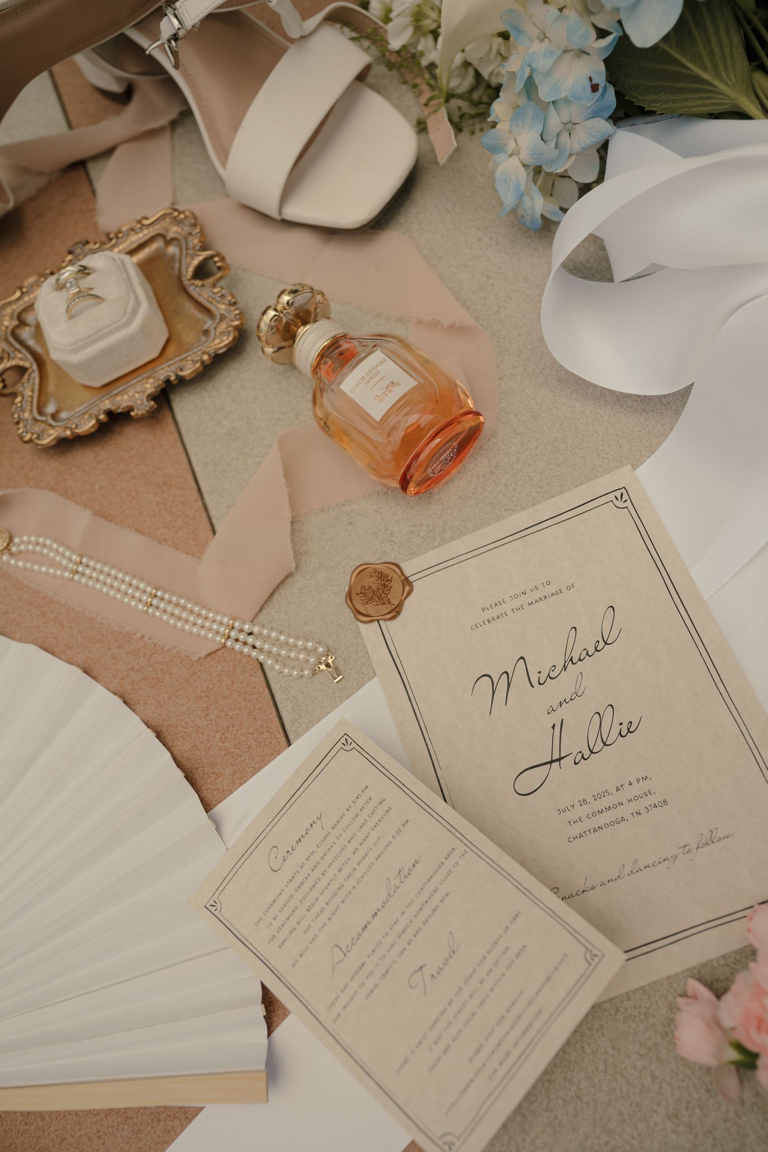 Elegant wedding flat lay with invitation, pearls, perfume, and hydrangeas.