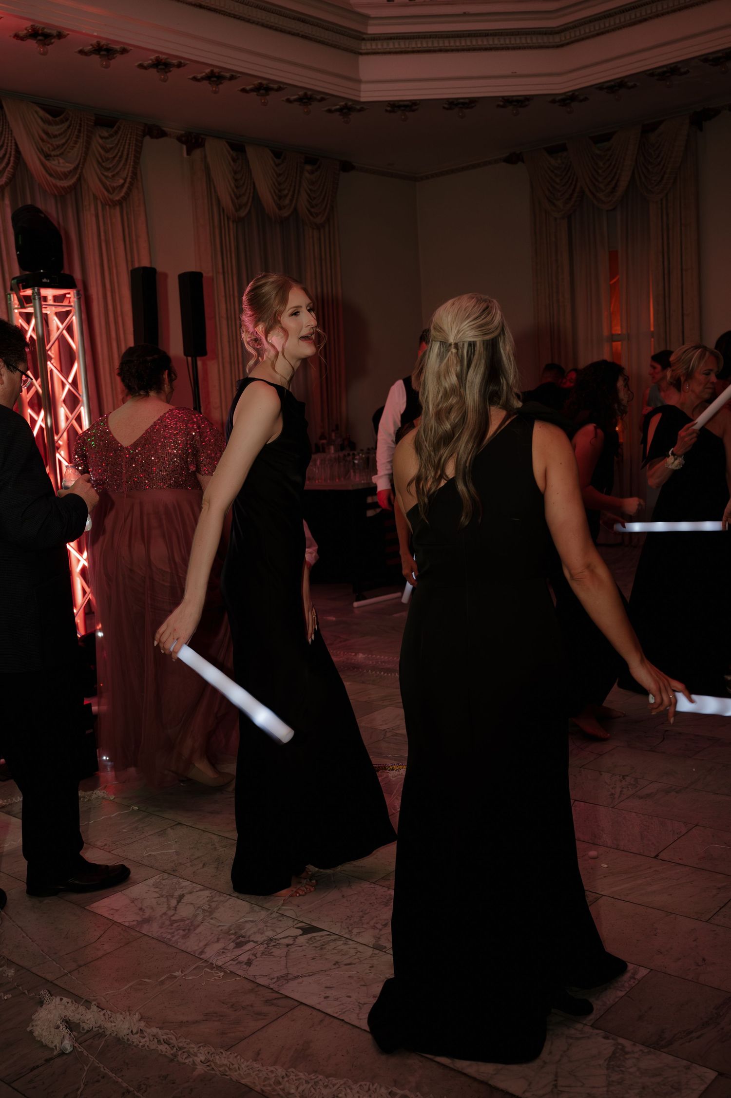 Two bridesmaids in black gowns dancing with light-up foam sticks at a formal wedding reception. Columbus Ohio Wedding at The Westin Hotel.