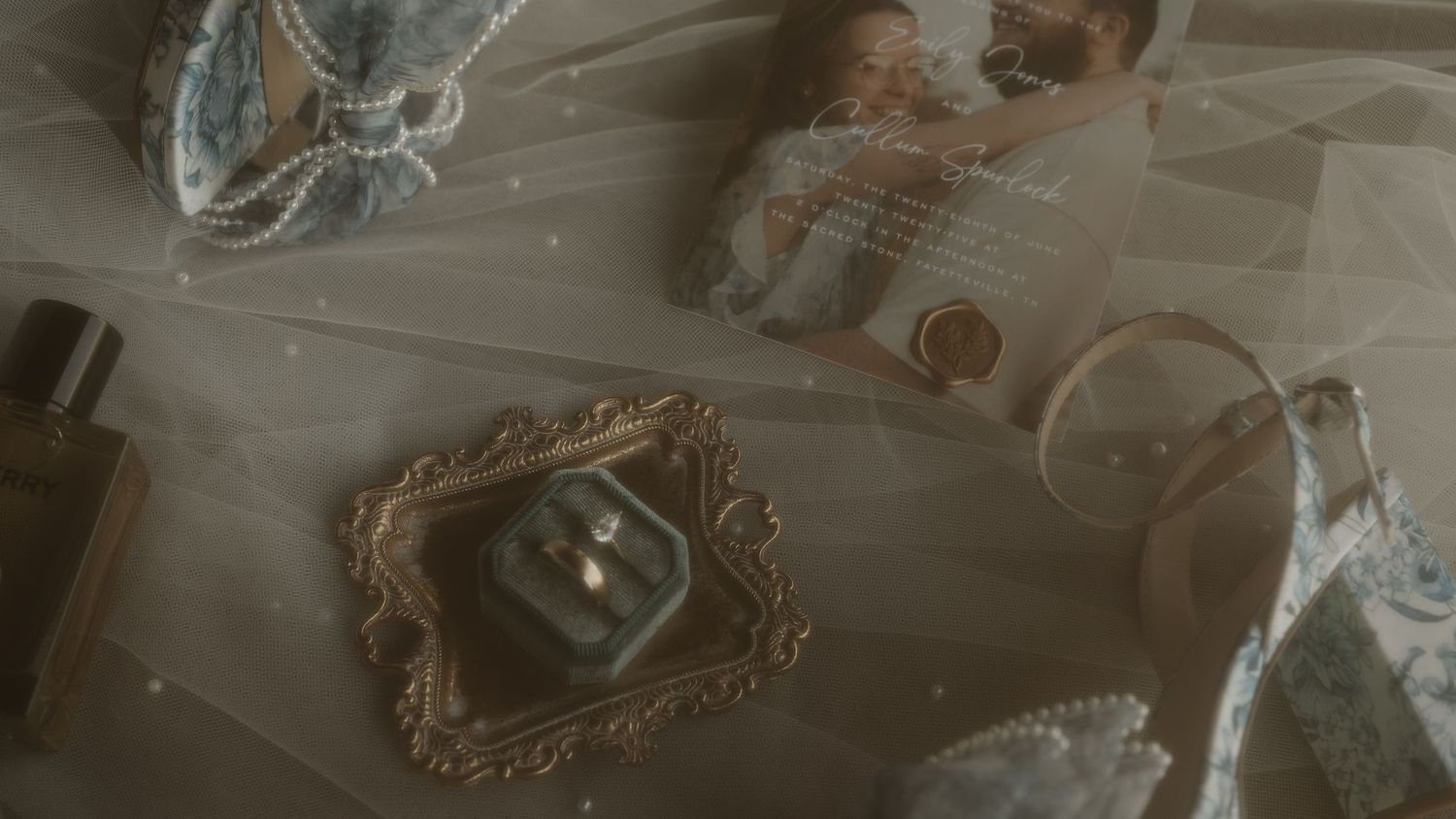 Overhead bridal flat lay with veil, ornate mirror, ring box, invitation, and perfume bottle details.