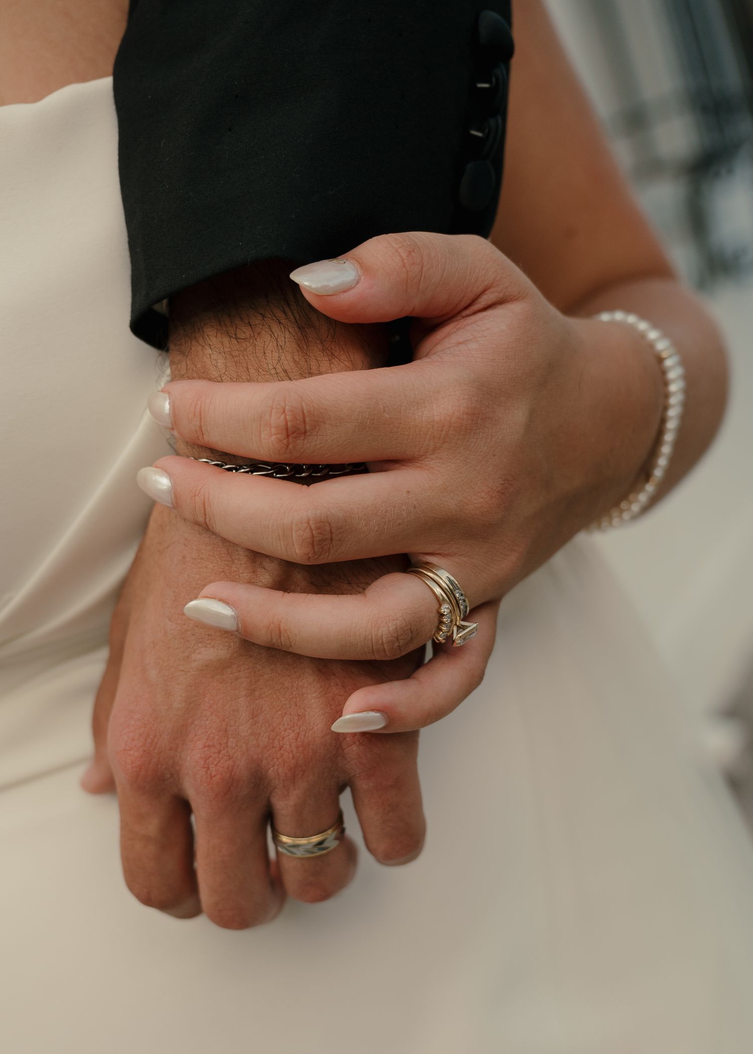Close-up of newlyweds hands intertwined showing wedding bands and pearl bracelet after ceremony.