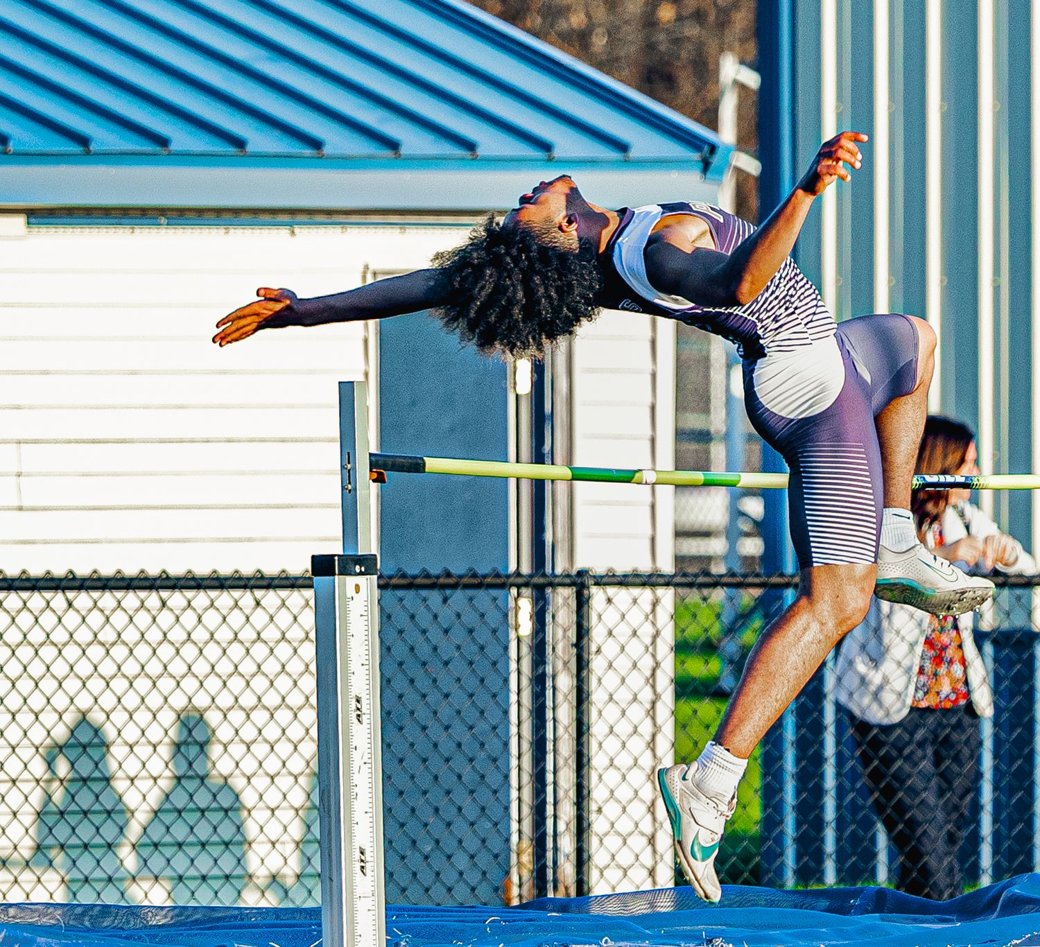 Female athlete performs high jump, arching back over bar in athletic competition outdoors.
