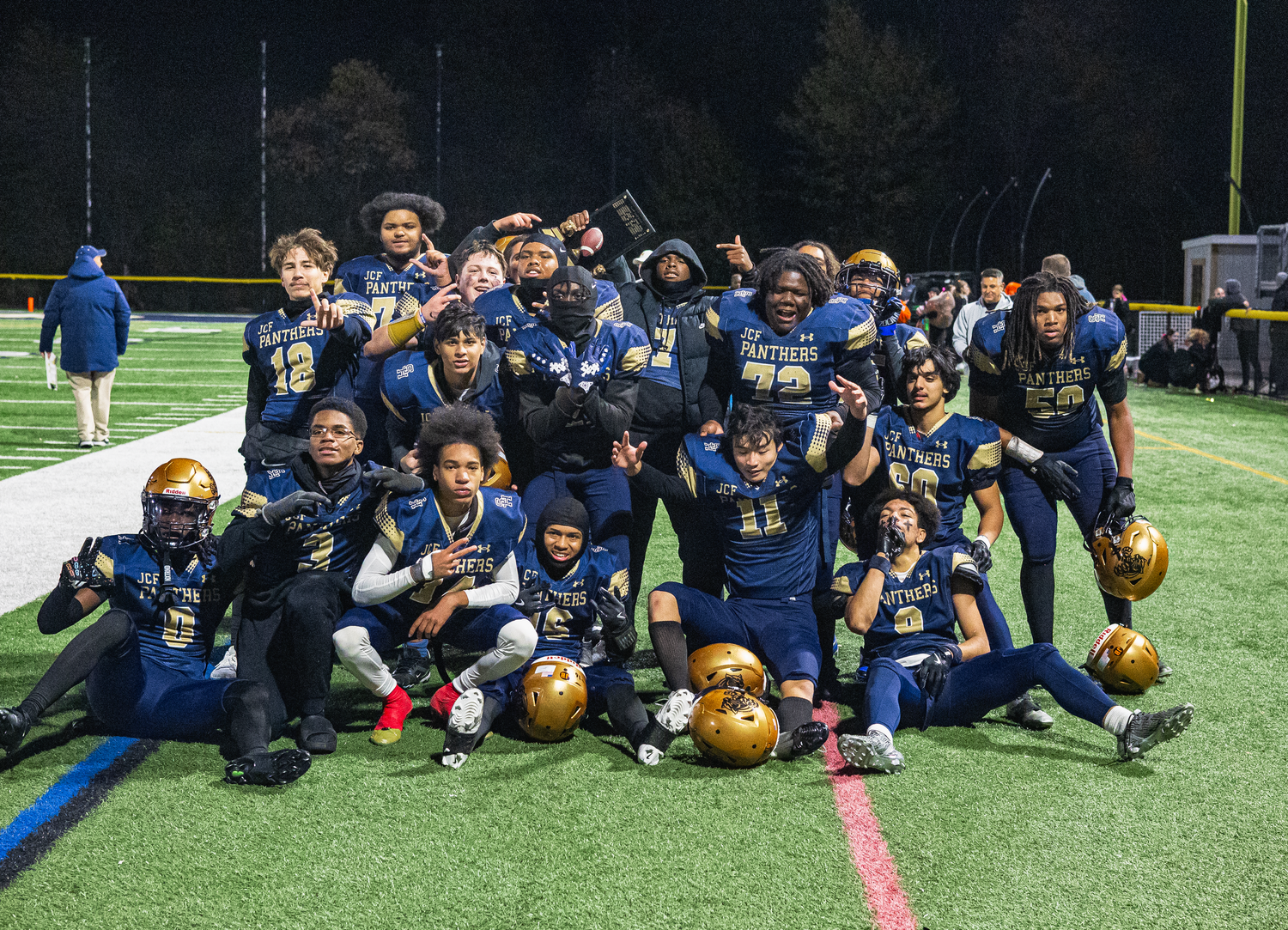 Youth football team poses together on field at night after a game win.