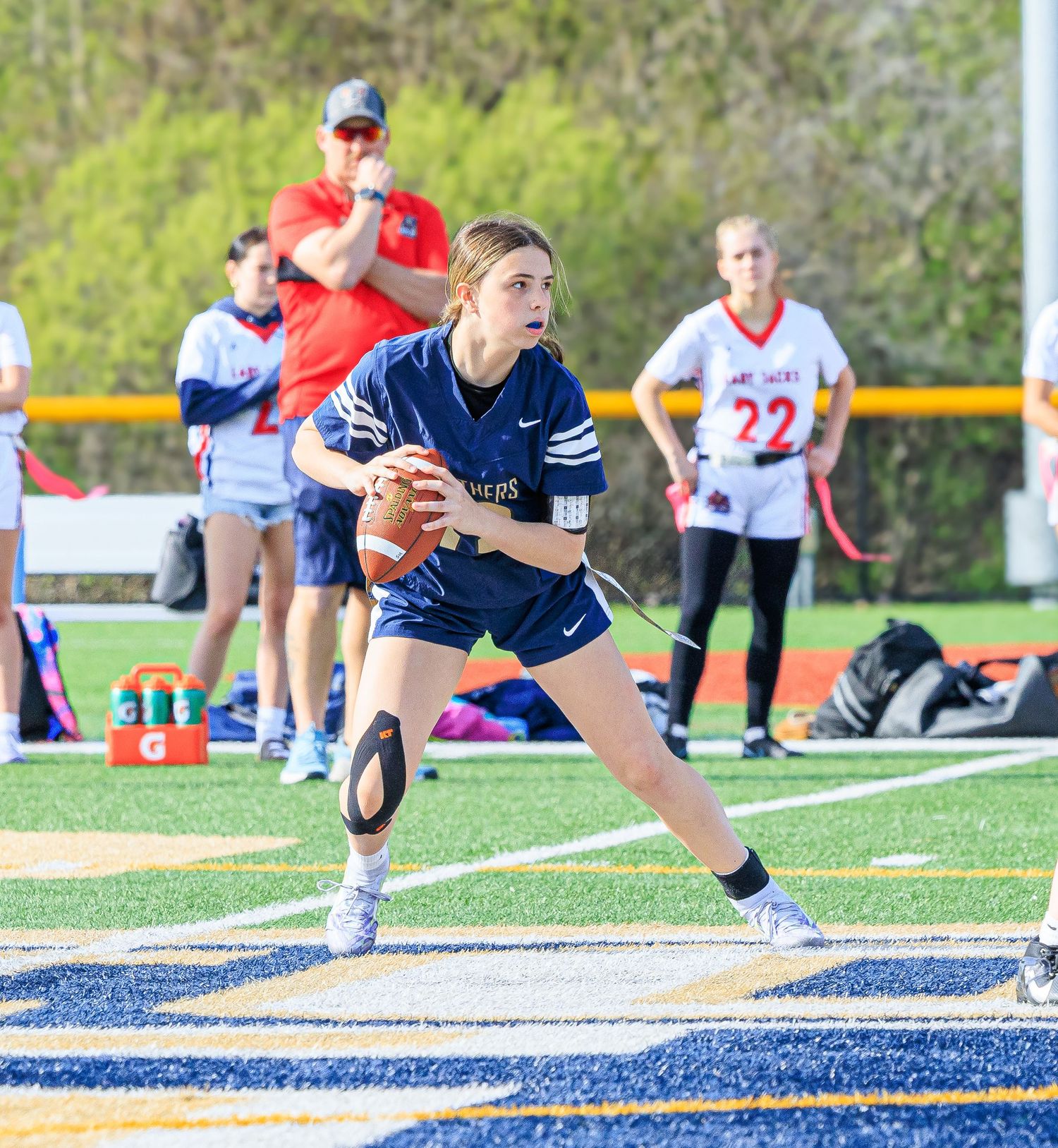 Female flag football player in navy uniform prepares to throw a pass during a high school game.