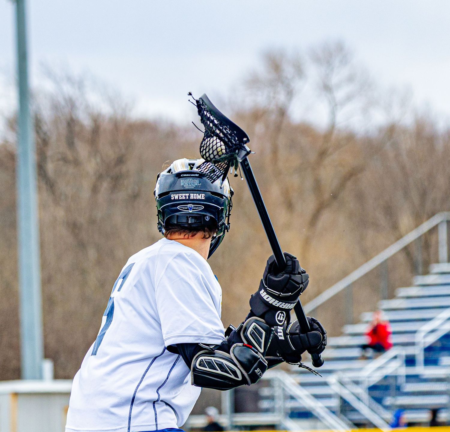 Lacrosse player in white uniform raising stick overhead during outdoor game.