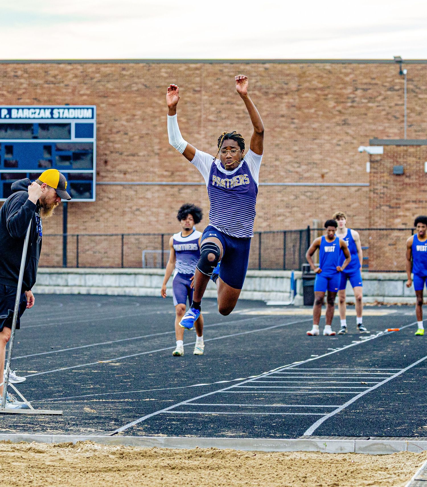 Athlete in purple Panthers uniform performs long jump at P. Barczak Stadium during a track and field meet.
