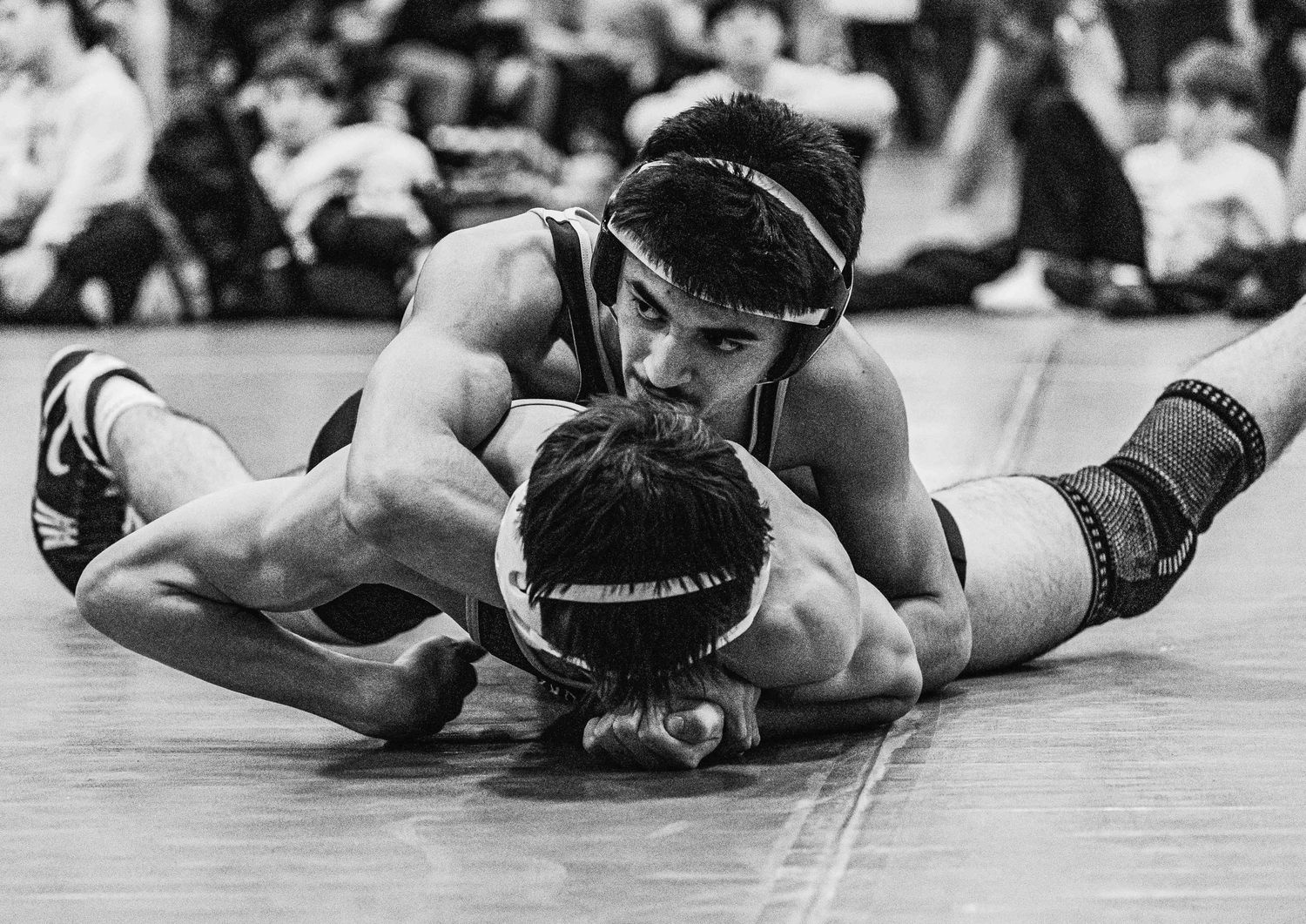 Two wrestlers compete in a high school or collegiate wrestling match on the mat in black and white photography.