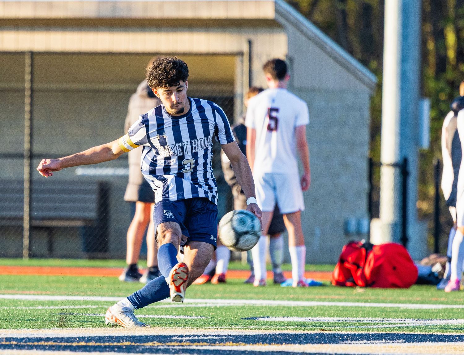 Soccer player in striped jersey kicking ball during high school match.