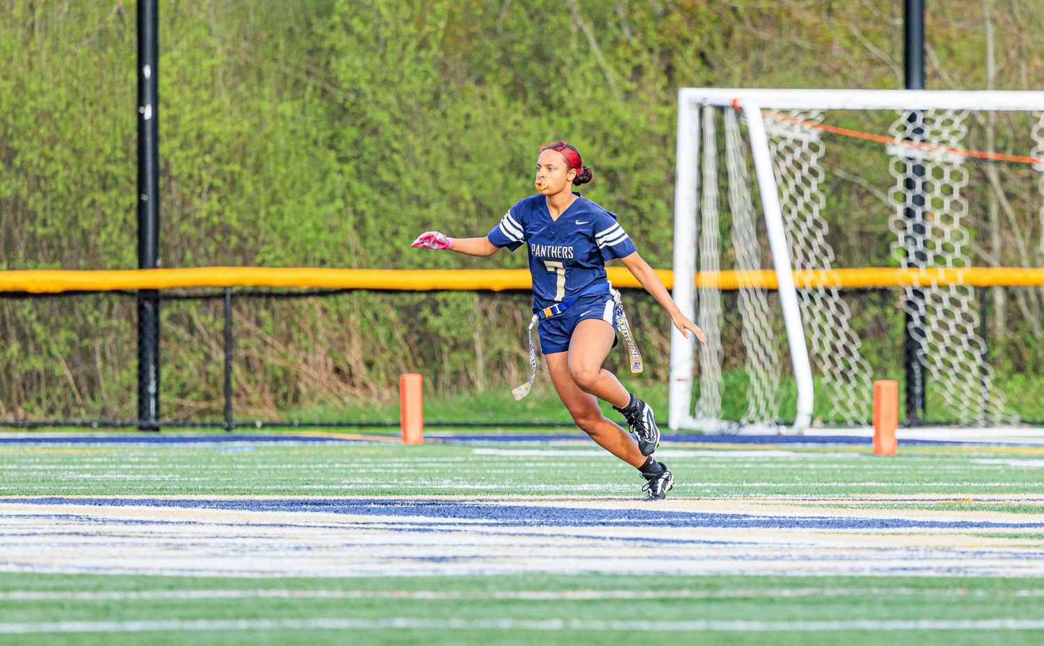 Female flag football player in navy uniform sprints down turf field during game.