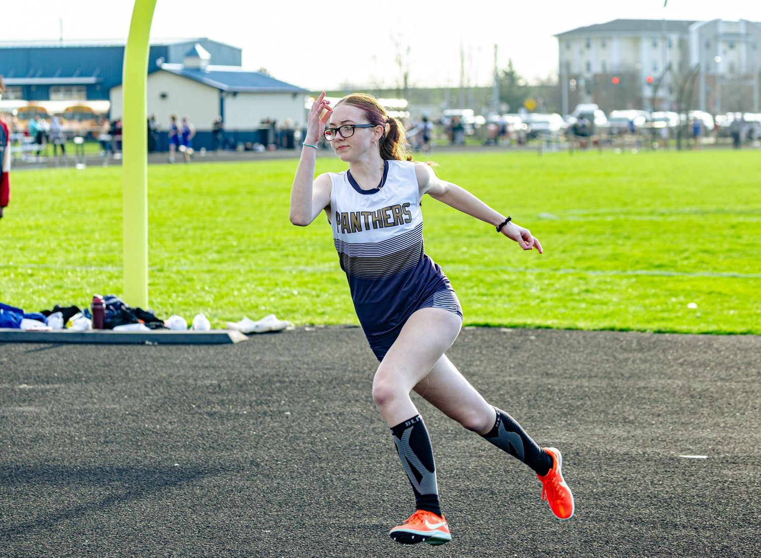 A female Panthers track athlete sprints down the track wearing glasses and orange shoes during an outdoor meet.