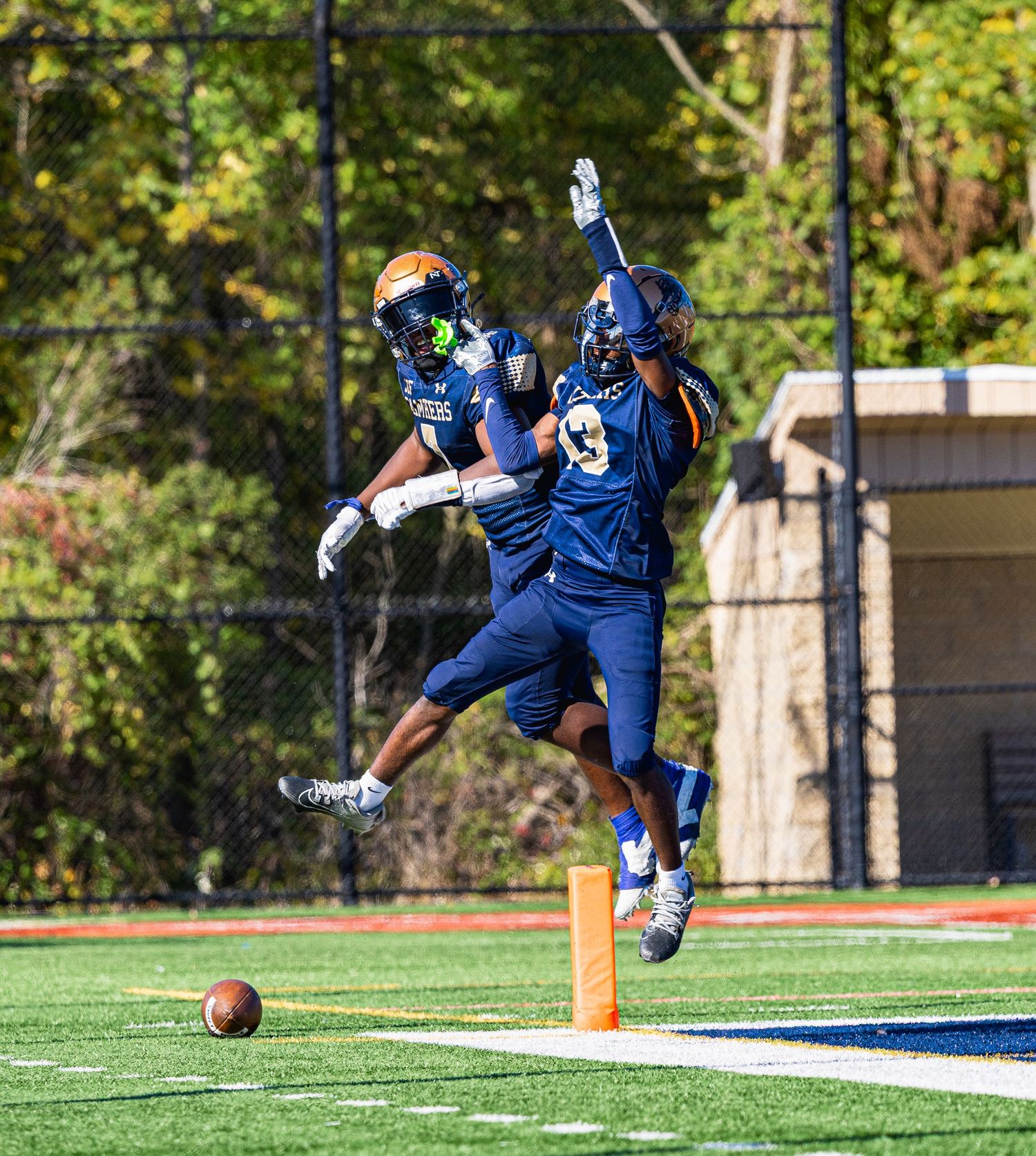 Football player in blue uniform dives dramatically towards the end zone during game play on artificial turf field.