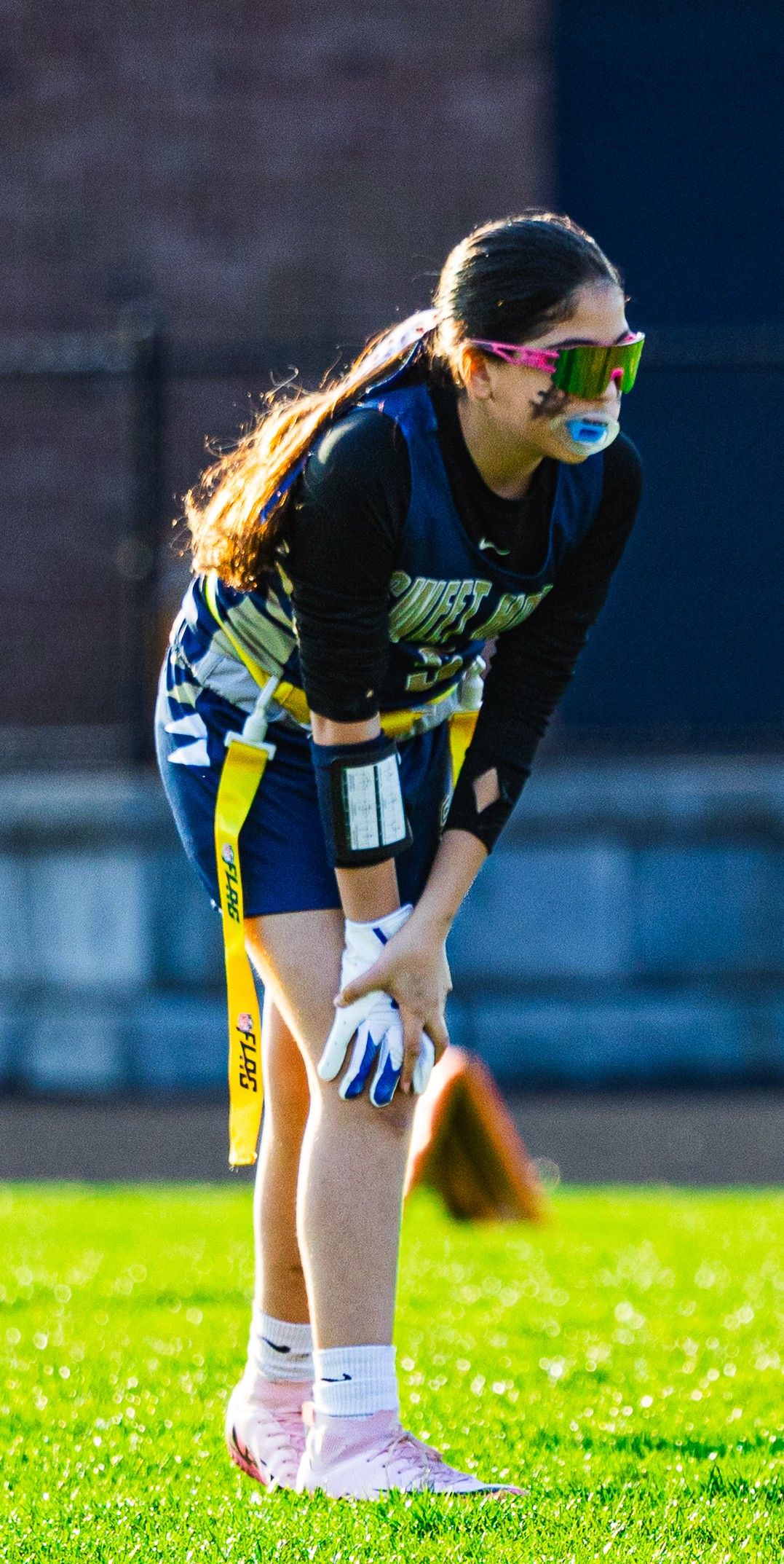 Softball player in navy and yellow uniform takes a break during game.