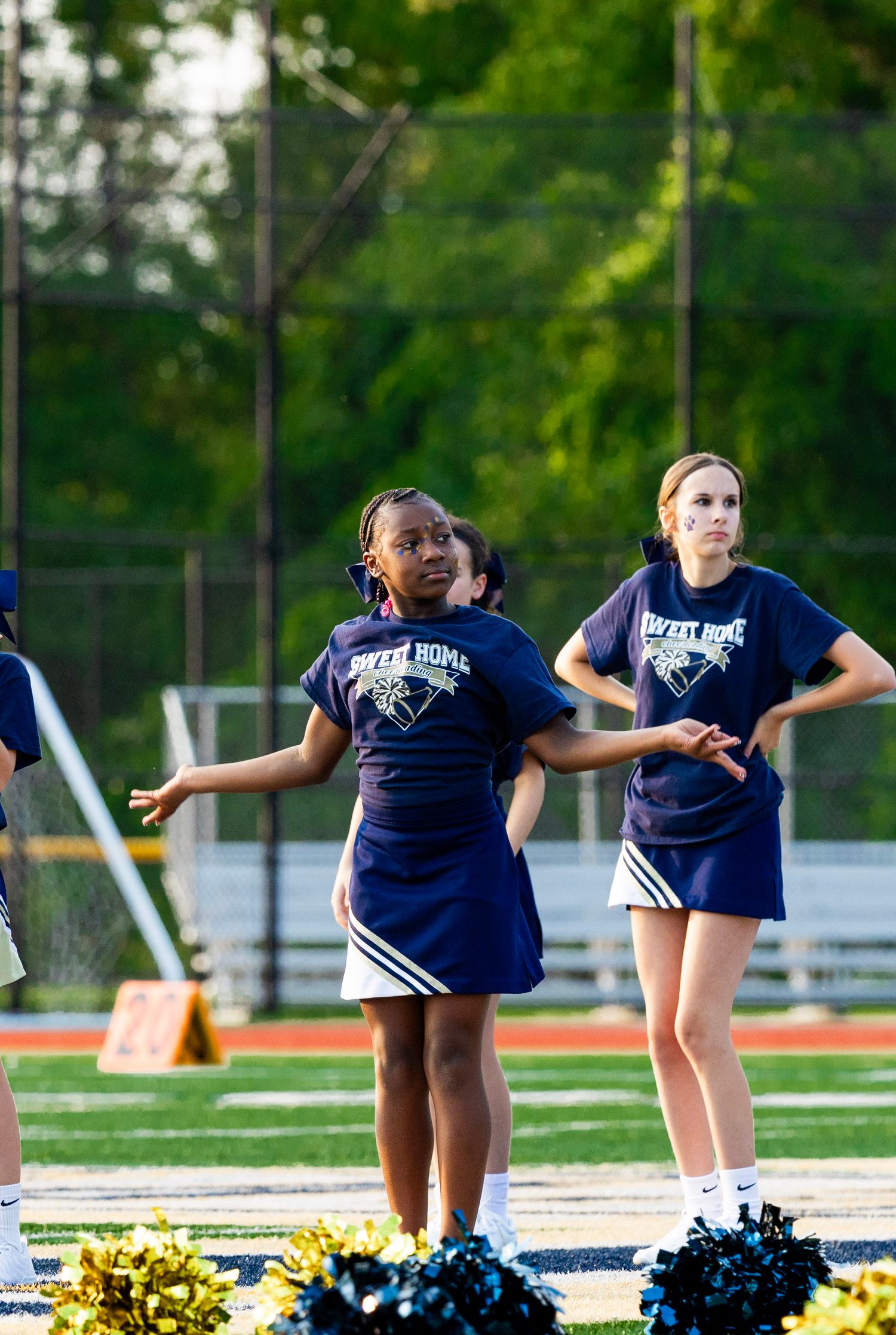 Cheerleaders in navy uniforms strike dynamic poses during field performance.
