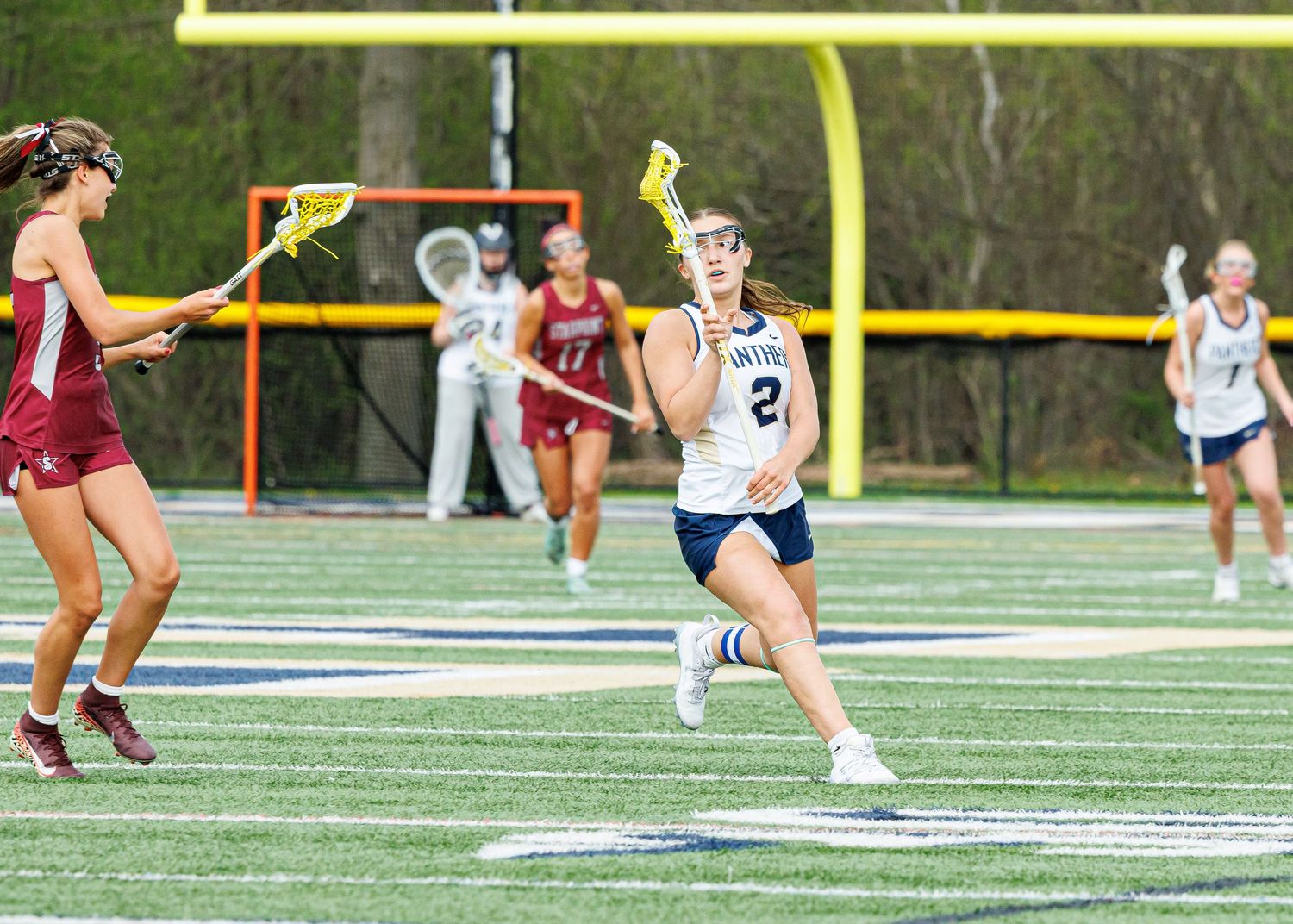 Panthers girls lacrosse player number 2 drives past opposing defender during competitive game on turf field.