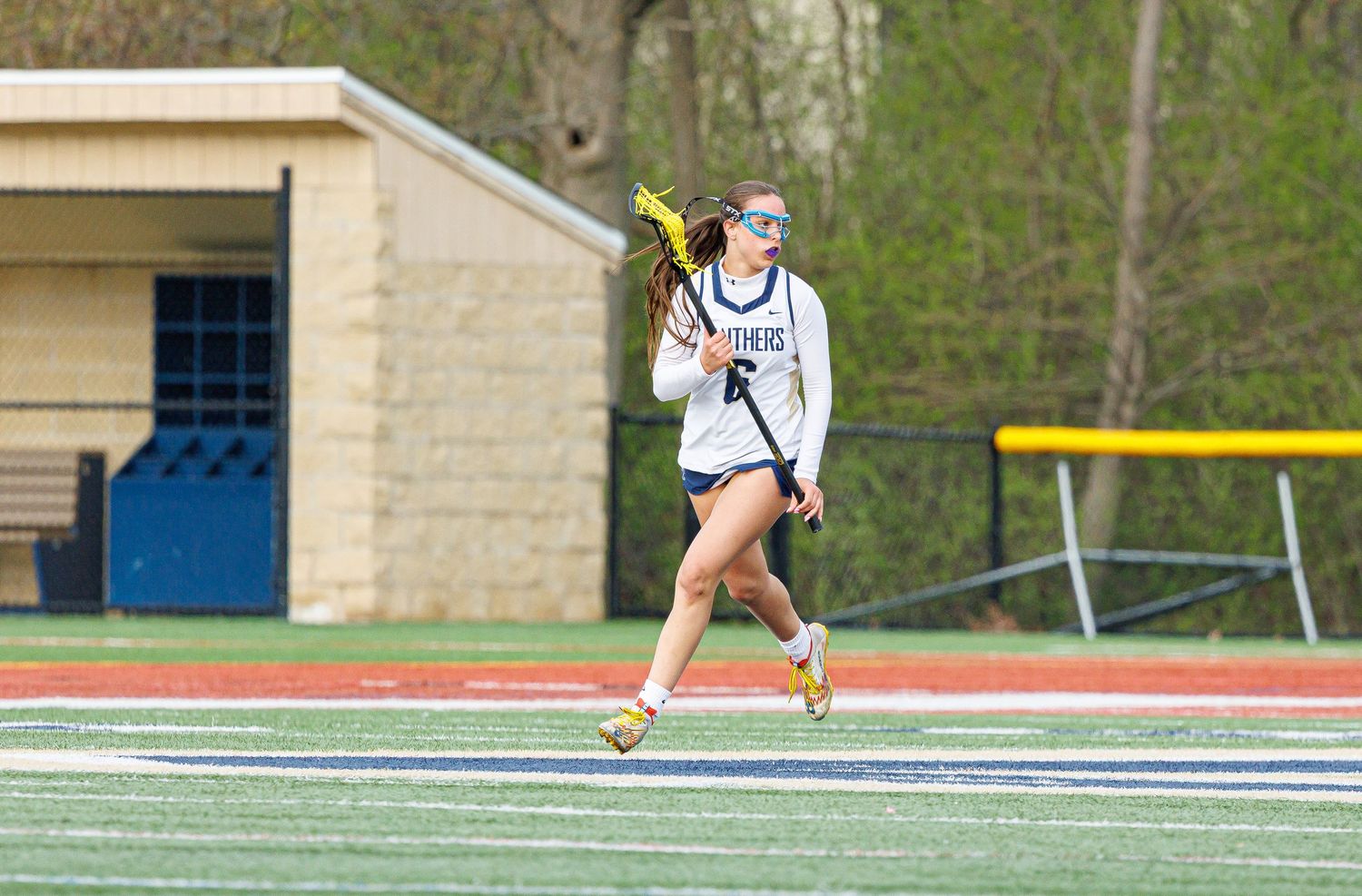 Female lacrosse player in white uniform running on field, cradling stick during outdoor spring game.