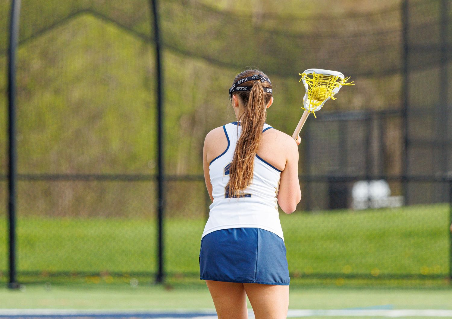 Female lacrosse player holds stick ready during an outdoor girls lacrosse game on a blue court.