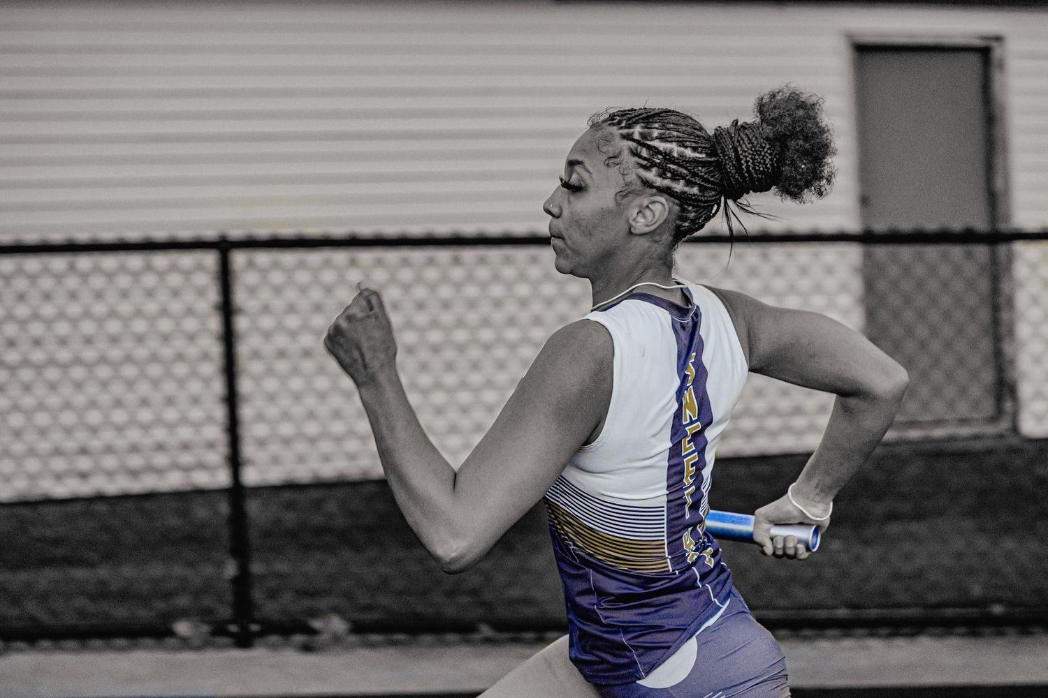 Female sprinter running in blue and gold uniform during a track and field competition.