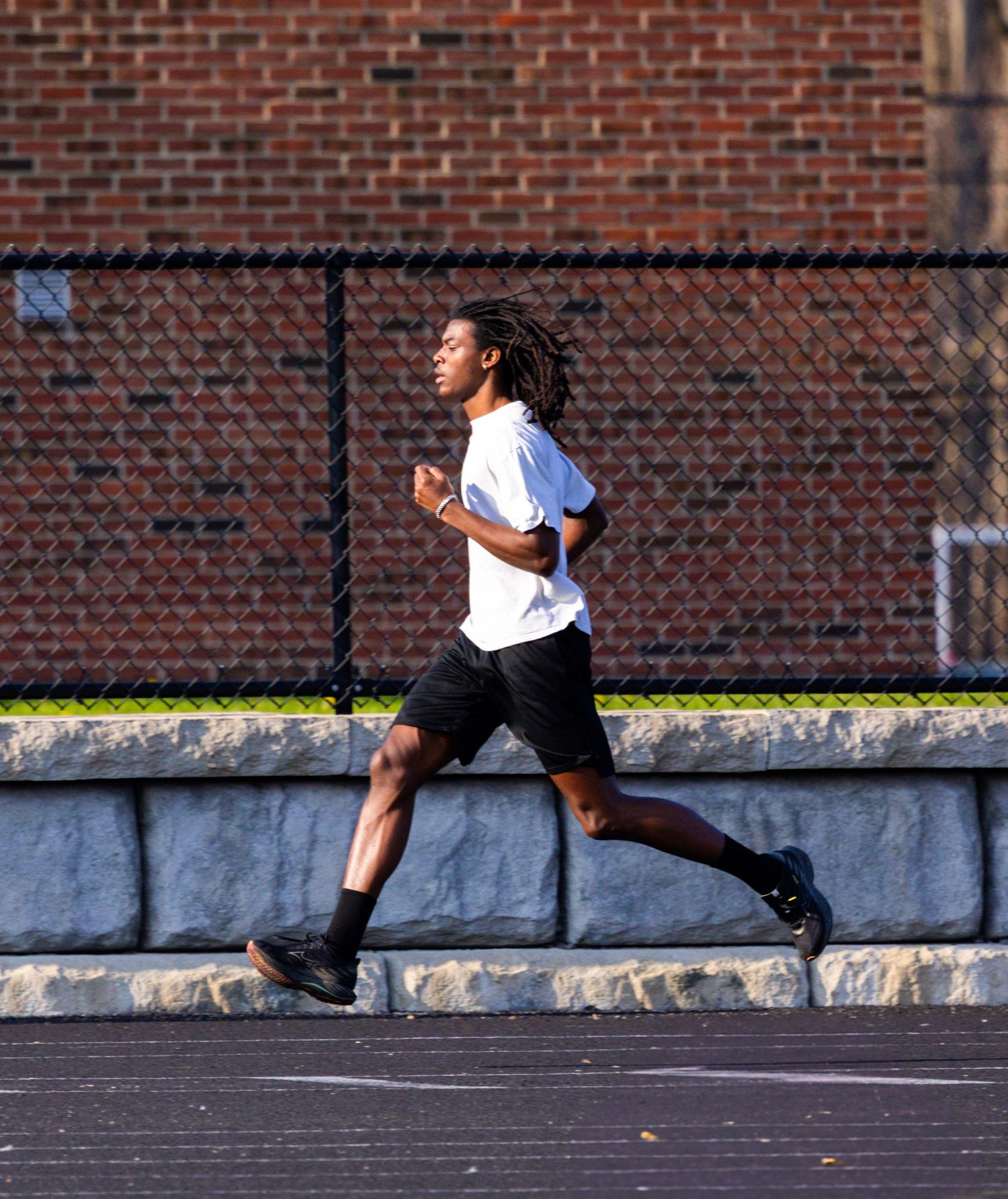 Runner sprints along track with brick wall and fence in background.