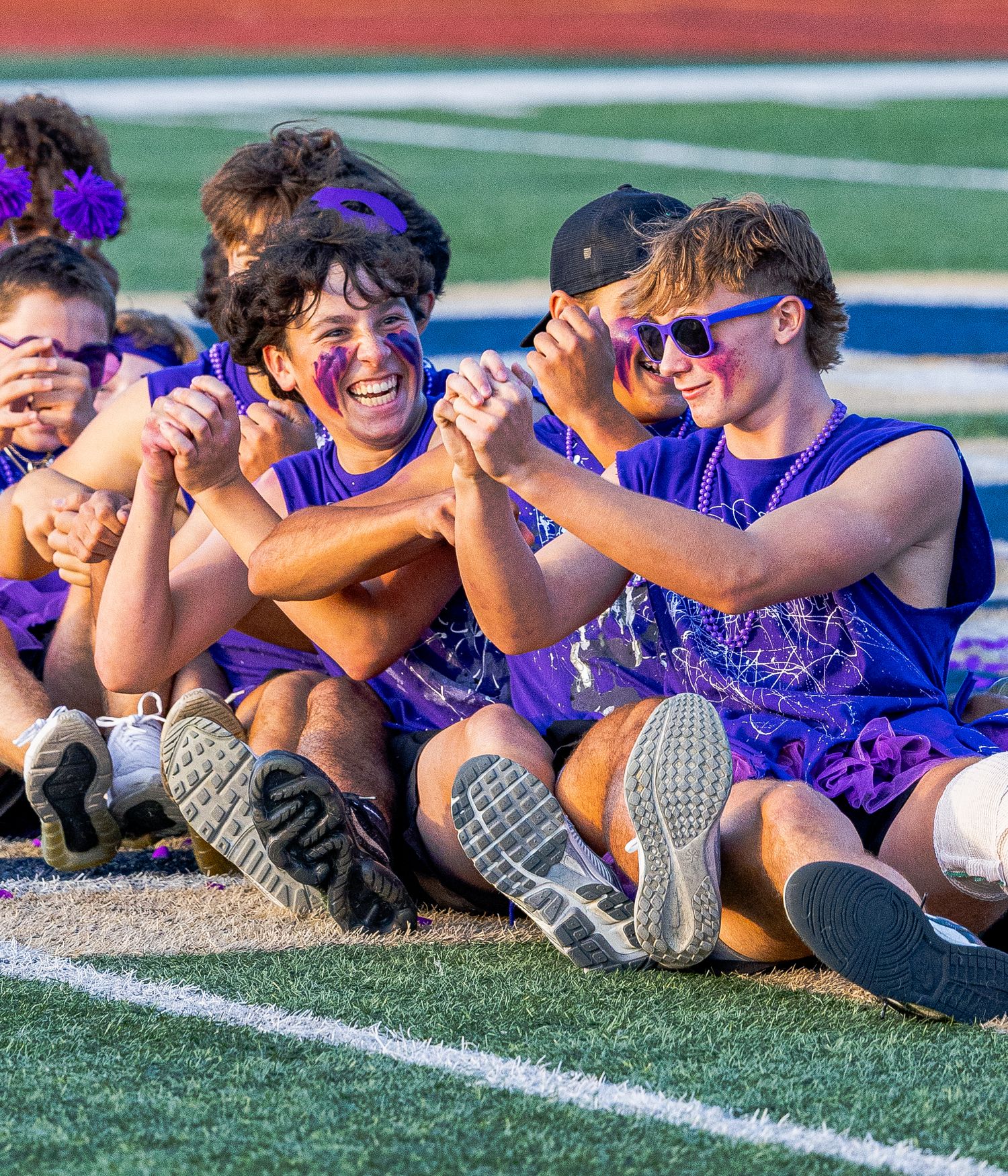 Athletes relax and laugh together while lying on the turf field during a sunny day at practice.