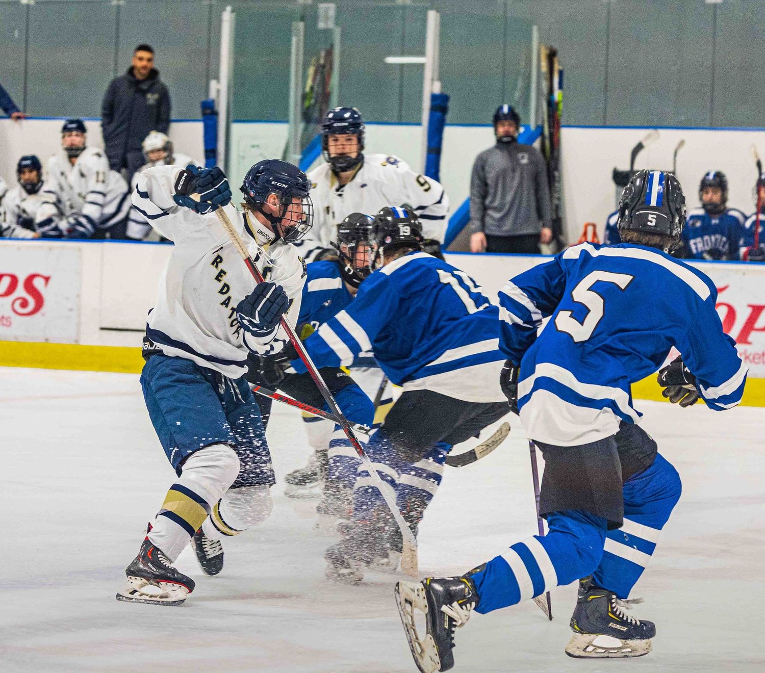 Ice hockey players in blue and white uniforms battle for the puck during an intense game on an indoor rink.